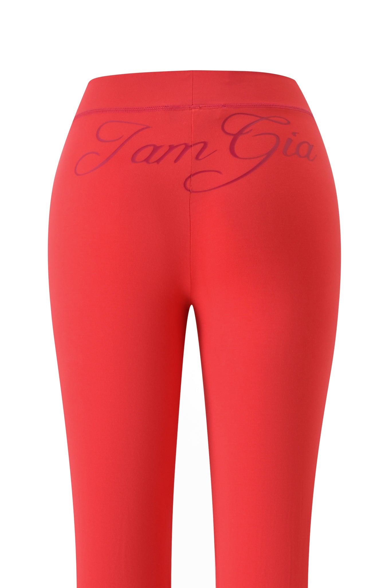 The BLARE TRACKPANT - PAPAYA by I.AM.GIA is shown from the back, with bold purple “I.AM.GIA” cursive lettering across the high-waisted waistband. The bright red leggings are set against a plain white background.