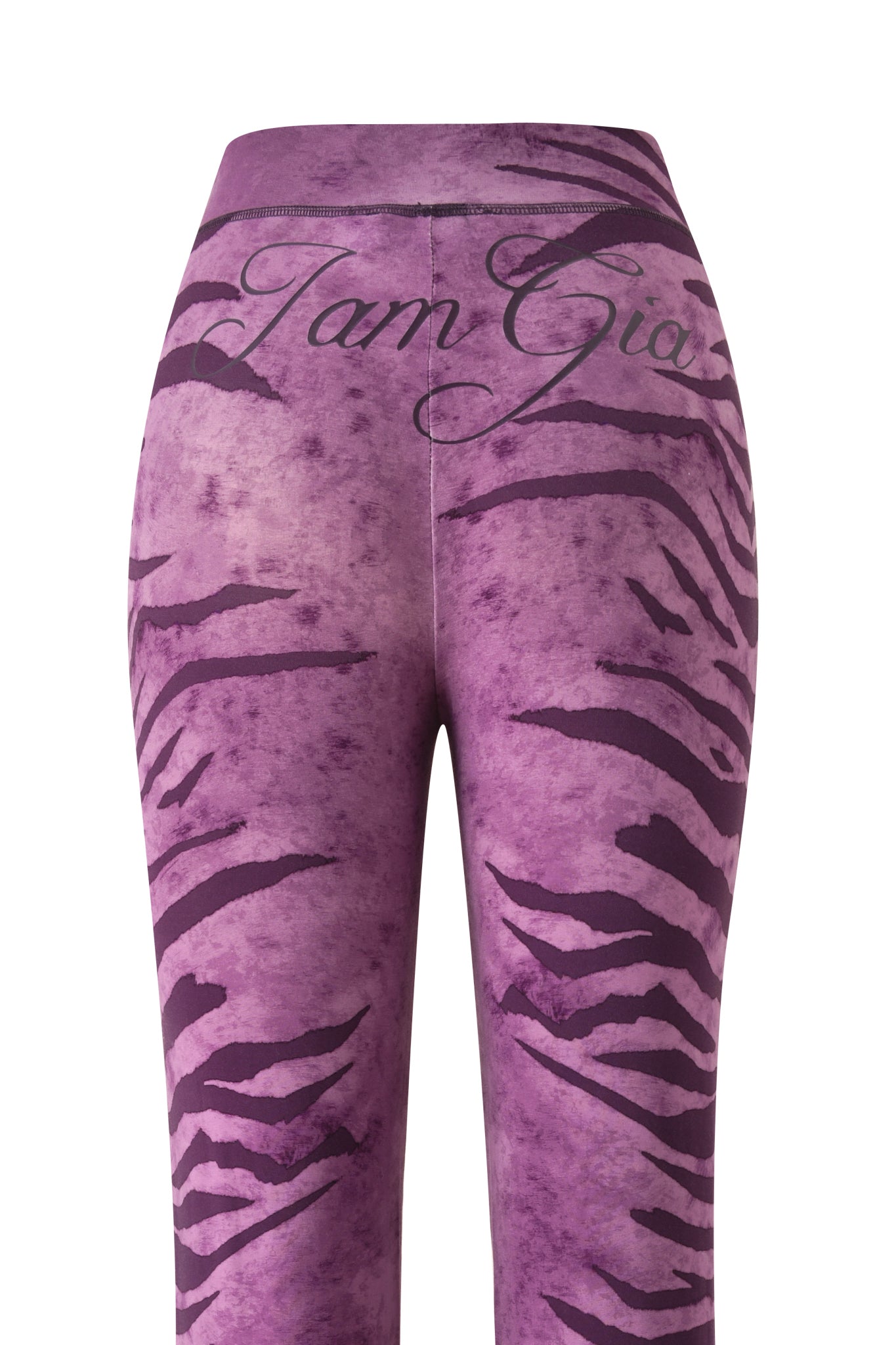 The BLARE TRACKPANT - PLUM WILD SIDE by I.AM.GIA features a purple tiger stripe design, cursive branding on the waistband, and flared legs. The image highlights the back view of these bold trackpant leggings.