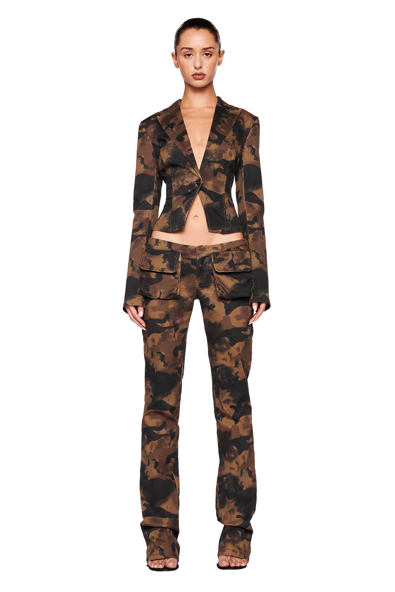 A person stands facing forward, wearing an I.AM.GIA camouflage-patterned suit jacket cropped just below the chest, paired with the KIMANI PANT - GREEN : CAMO. The outfit combines a formal look with a military-inspired print. The background is plain white.
