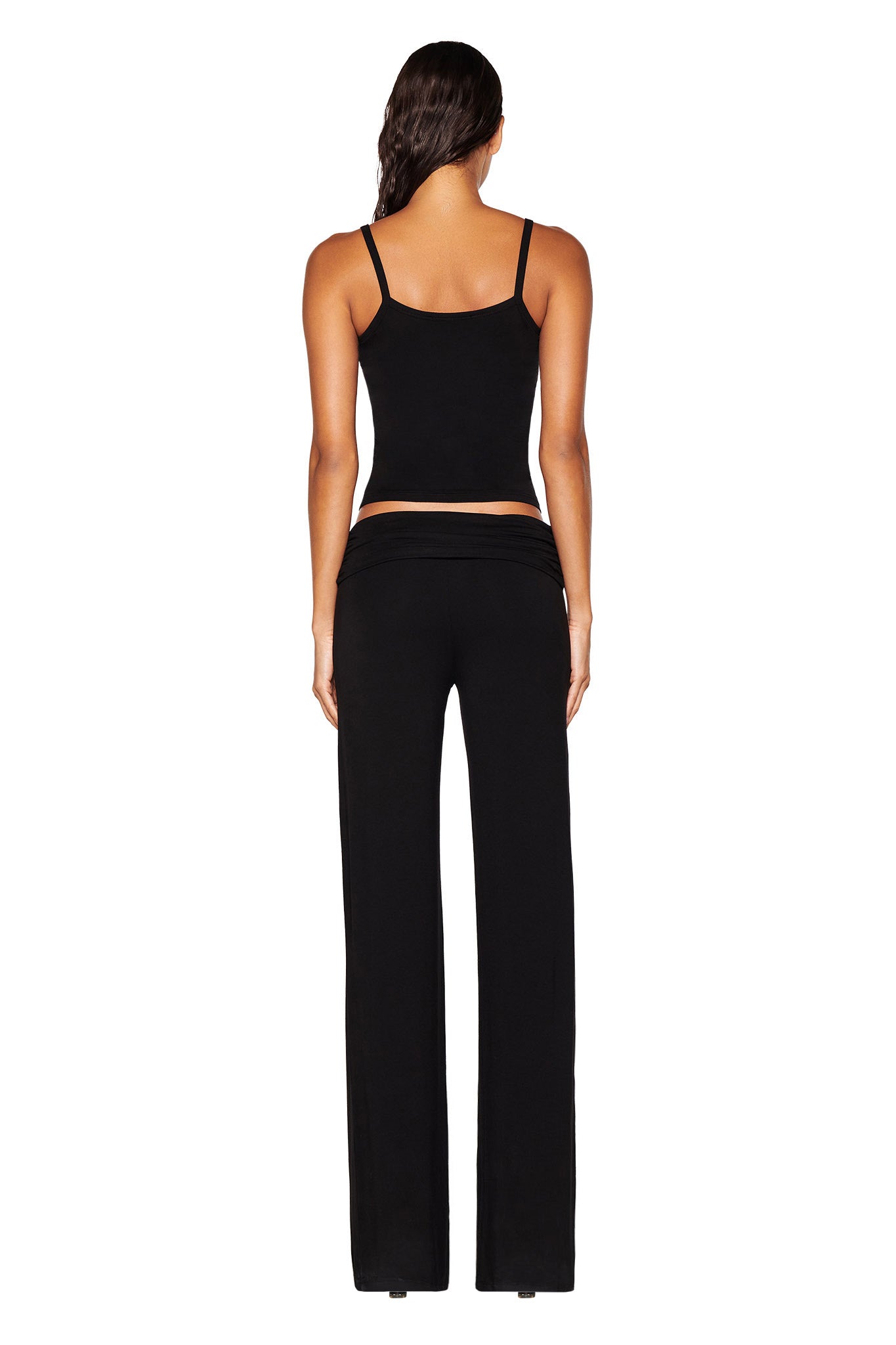 A person is facing away, wearing the ERIN TOP - BLACK by I.AM.GIA, paired with black wide-leg pants. Their long hair cascades down their back against a plain white background.