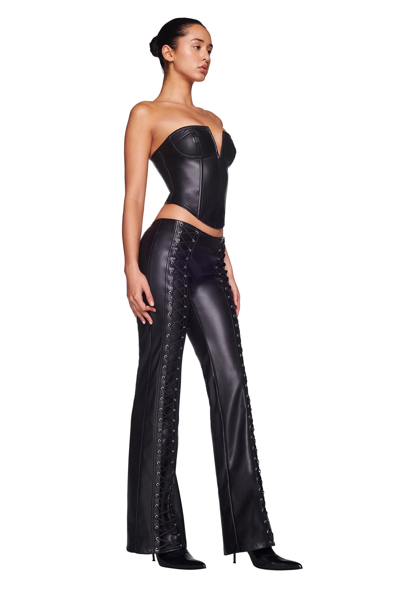 A person is posing in a fitted, strapless black leather top and I.AM.GIA's SONORA PANT - BLACK featuring lace-up details along the sides. They are wearing black heeled boots, have their hair pulled back, and are standing against a plain white background.