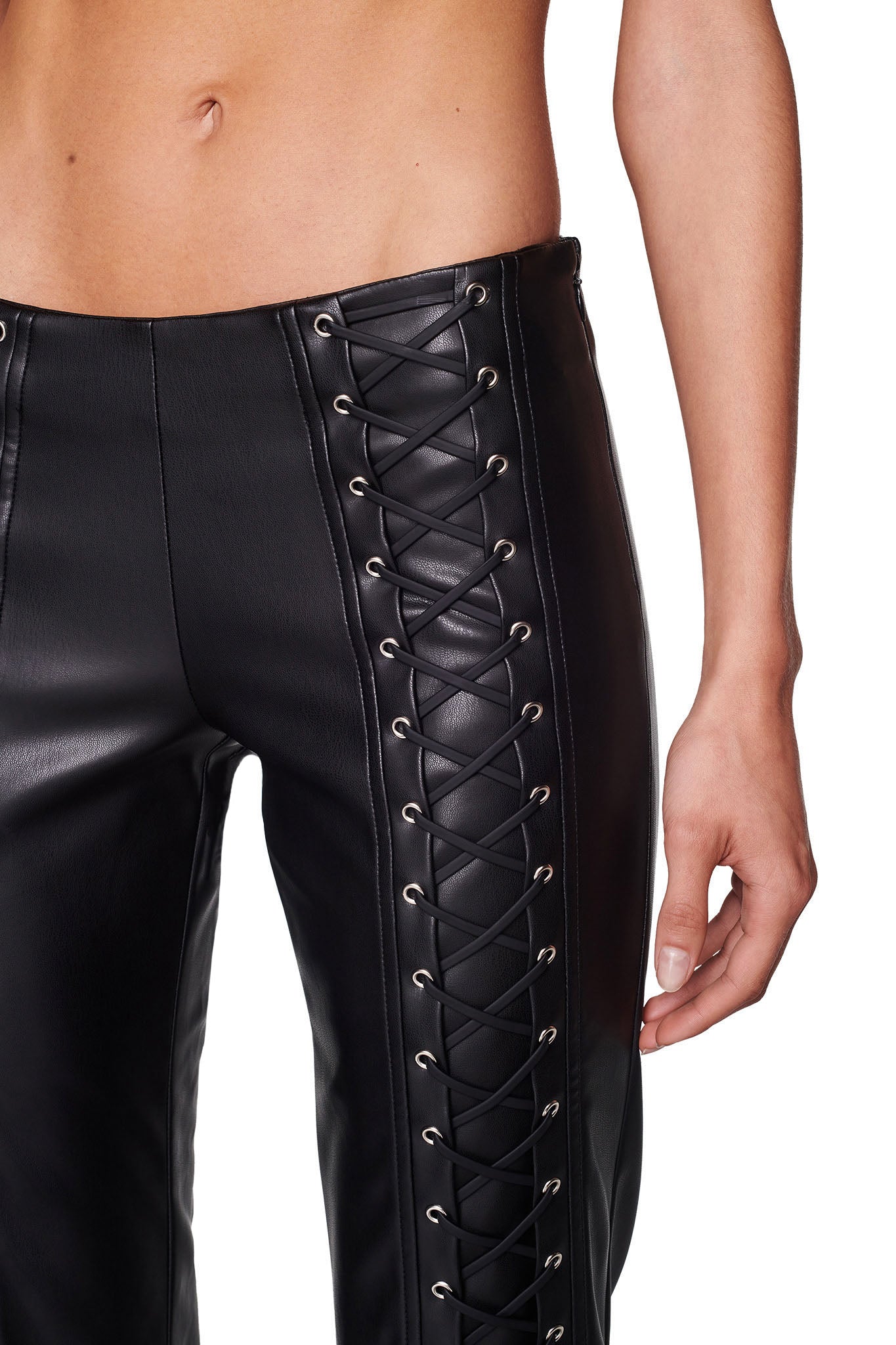Close-up of a person wearing the SONORA PANT - BLACK from I.AM.GIA, featuring crisscross lace-up details on the sides. The image focuses on the lower torso and upper legs, with the person's hand resting by their side. Their bare midriff is visible at the top of the image.