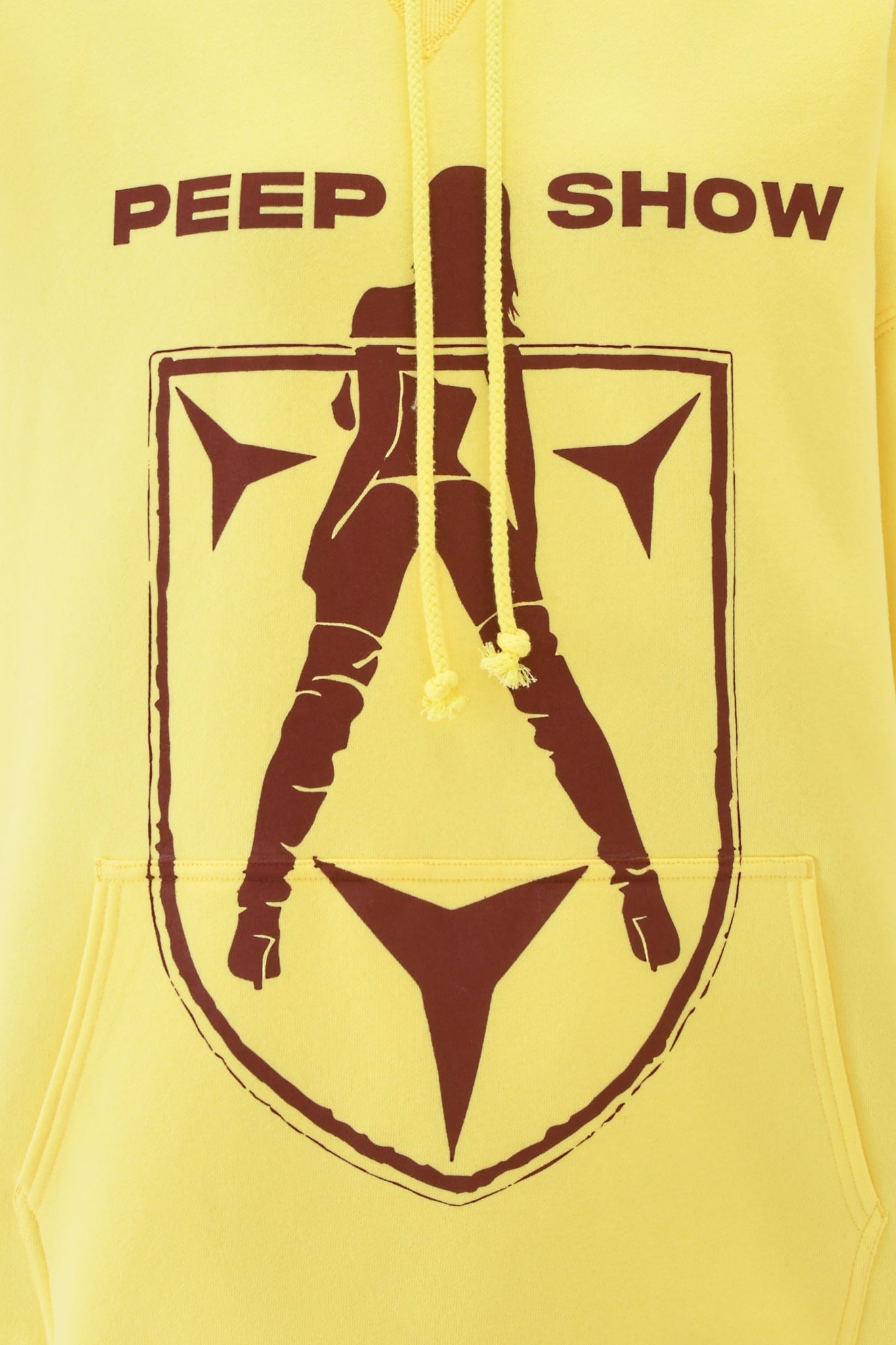The I.AM.GIA DORIAN HOODIE - YELLOW features “PEEP SHOW” in bold brown letters above a brown silhouette of a high-booted woman over a shield with abstract shapes.