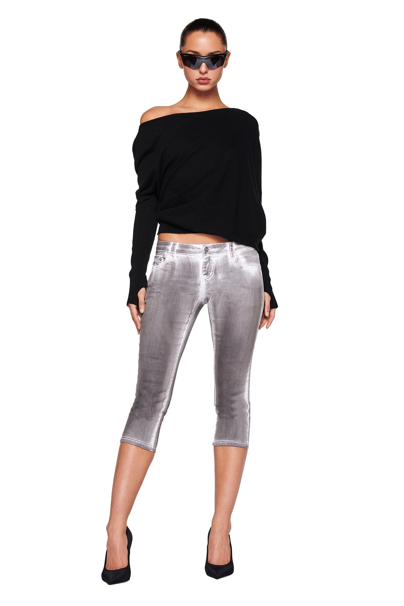 A woman is wearing the GISELLE TOP in black from I.AM.GIA, silver metallic capri pants also by I.AM.GIA, black high-heeled shoes, and dark sunglasses. She stands with her legs slightly apart, hands by her sides, and gazes straight ahead. The background is plain white.