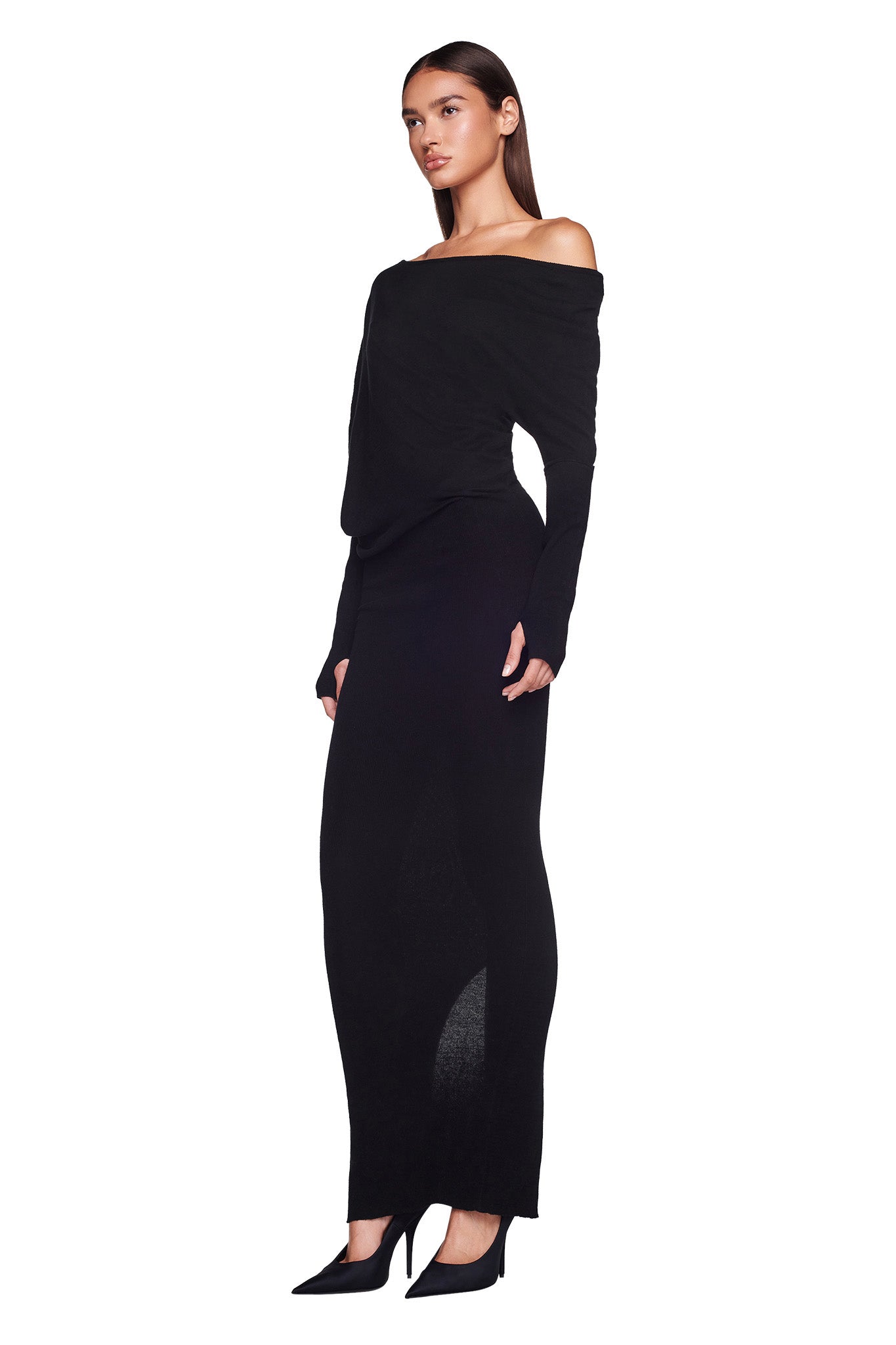 A woman stands against a white background, wearing the GISELLE MAXI DRESS from I.AM.GIA, an off-the-shoulder, long-sleeved black dress that extends to the floor. She is looking slightly to the left with her hands resting by her sides and wears black pointed-toe heels.
