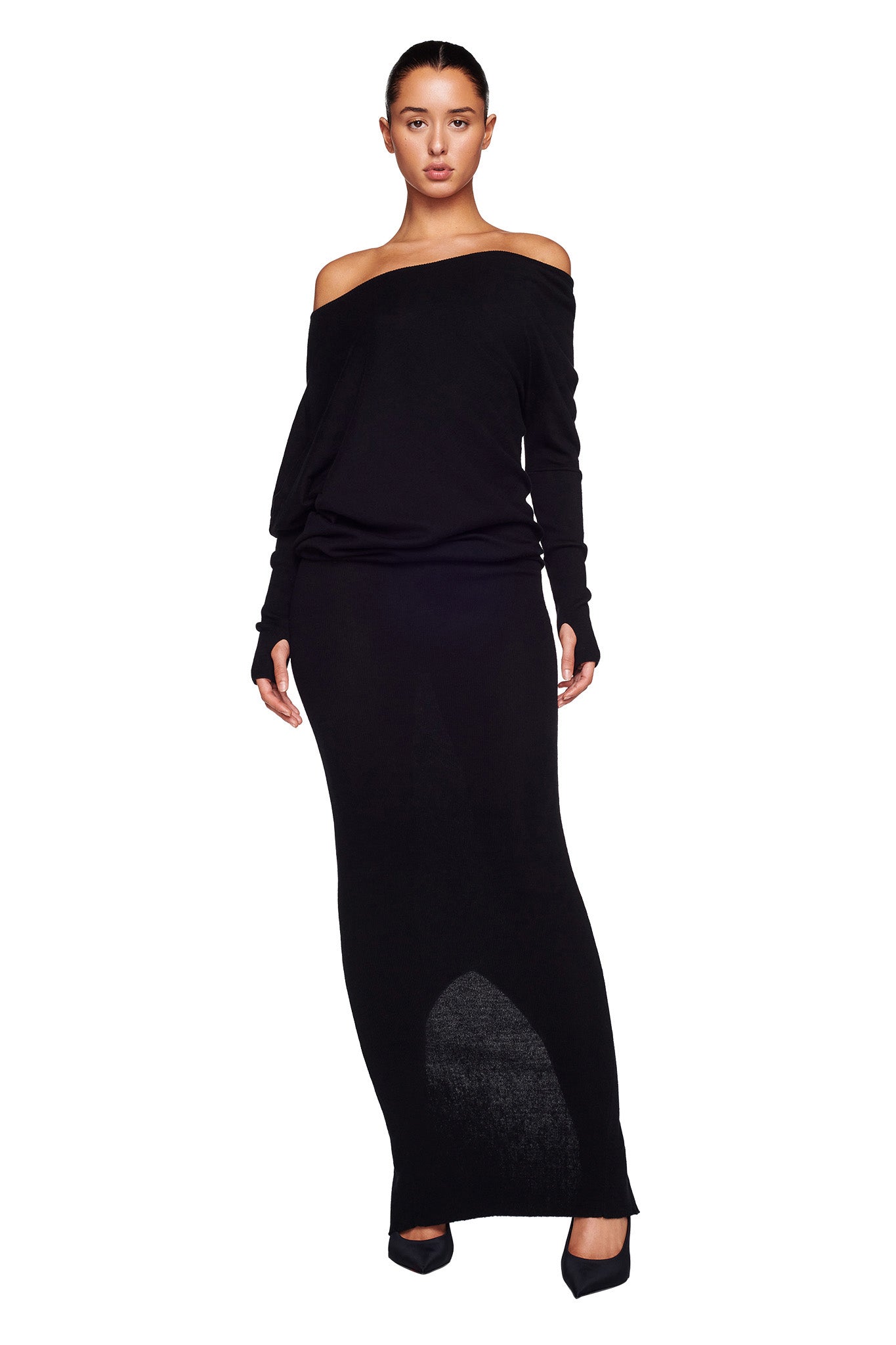 A woman stands facing forward wearing the GISELLE MAXI DRESS - BLACK by I.AM.GIA, an off-the-shoulder, long-sleeved dress that extends to her feet. She pairs the dress with black heels. Her hair is pulled back, and she has a neutral facial expression against a plain white background.