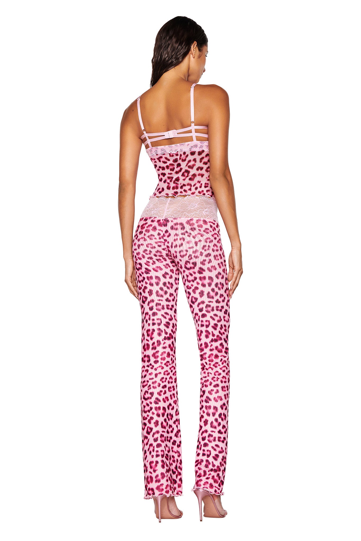 An individual showcases the I.AM.GIA 'SILO PANT - PINK : LEOPARD : PINK LEOPARD', a matching ensemble with a pink leopard print top and low-rise, straight-leg pants, highlighted by sheer panels at the waist and back. The model stands facing away with hands at their sides against a white backdrop.