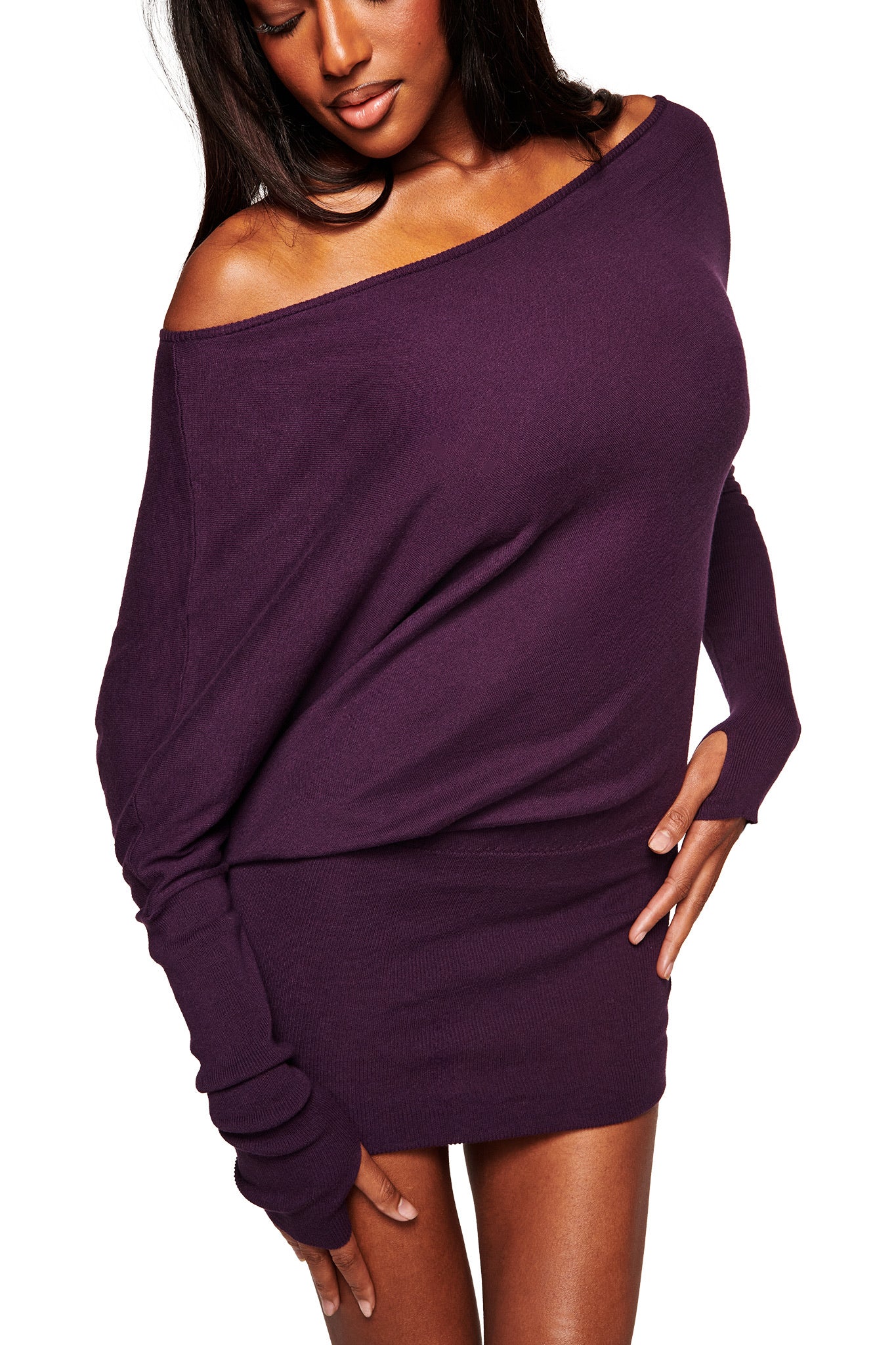 A woman poses confidently in the I.AM.GIA GISELLE MINI DRESS - PLUM, a fitted, off-the-shoulder sweater dress with long sleeves and a bold purple color, standing against a white background with one hand on her hip.