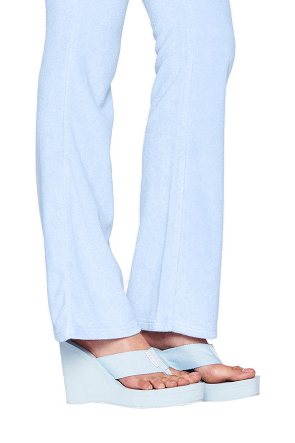 A person wearing light blue I.AM.GIA pants and matching SHELBY FLIP FLOP - BLUE : BABY BLUE platform flip-flops. The pants are slightly flared, and the footwear has thick, raised soles giving added height. The white background highlights the outfit and footwear.