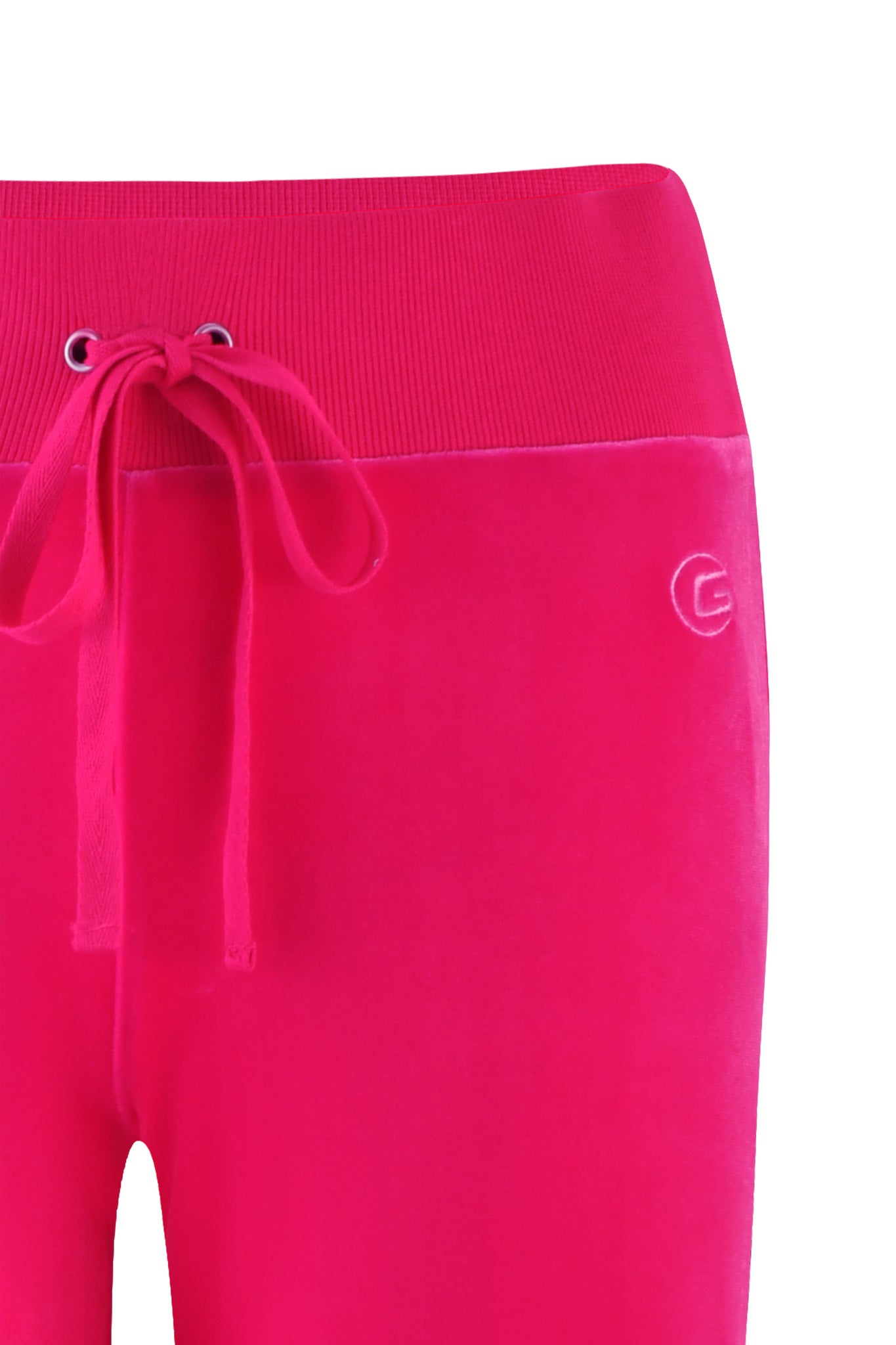 A close-up of the I.AM.GIA STACEY VELOUR PANT in hot pink, showcasing their bright hue and soft, plush fabric that subtly reflects light. The pants feature a ribbed waistband with a drawstring and metal eyelets, along with a small embroidered 'G' logo on the right side.