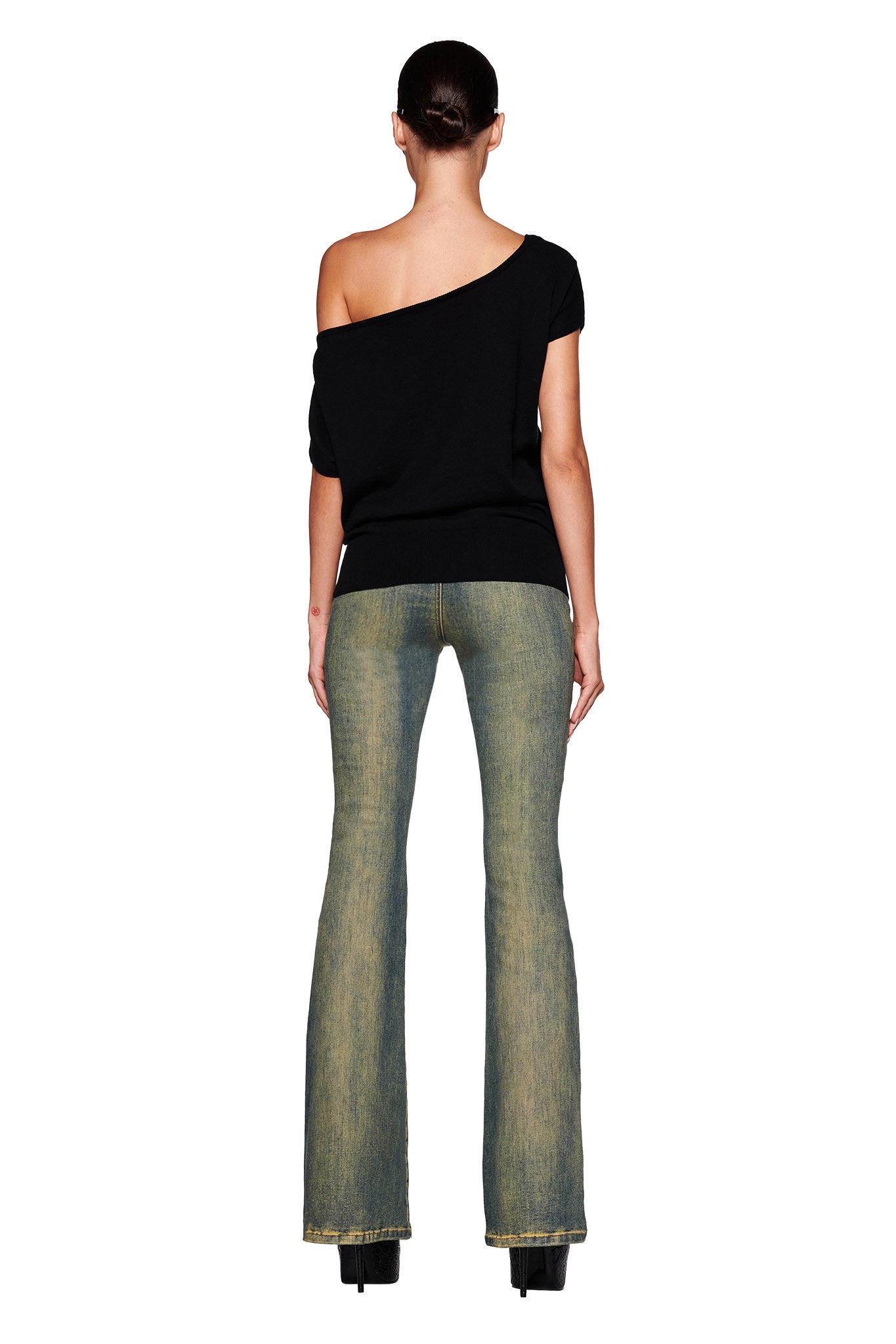 Rear view of a woman in the GISELLE SHORT SLEEVE TOP - BLACK by I.AM.GIA and high-waisted, flared blue jeans. Her brown hair is styled in a low bun, and she stands against a white background. She completes the look with black platform shoes, showcasing a sleek sleeveless silhouette.