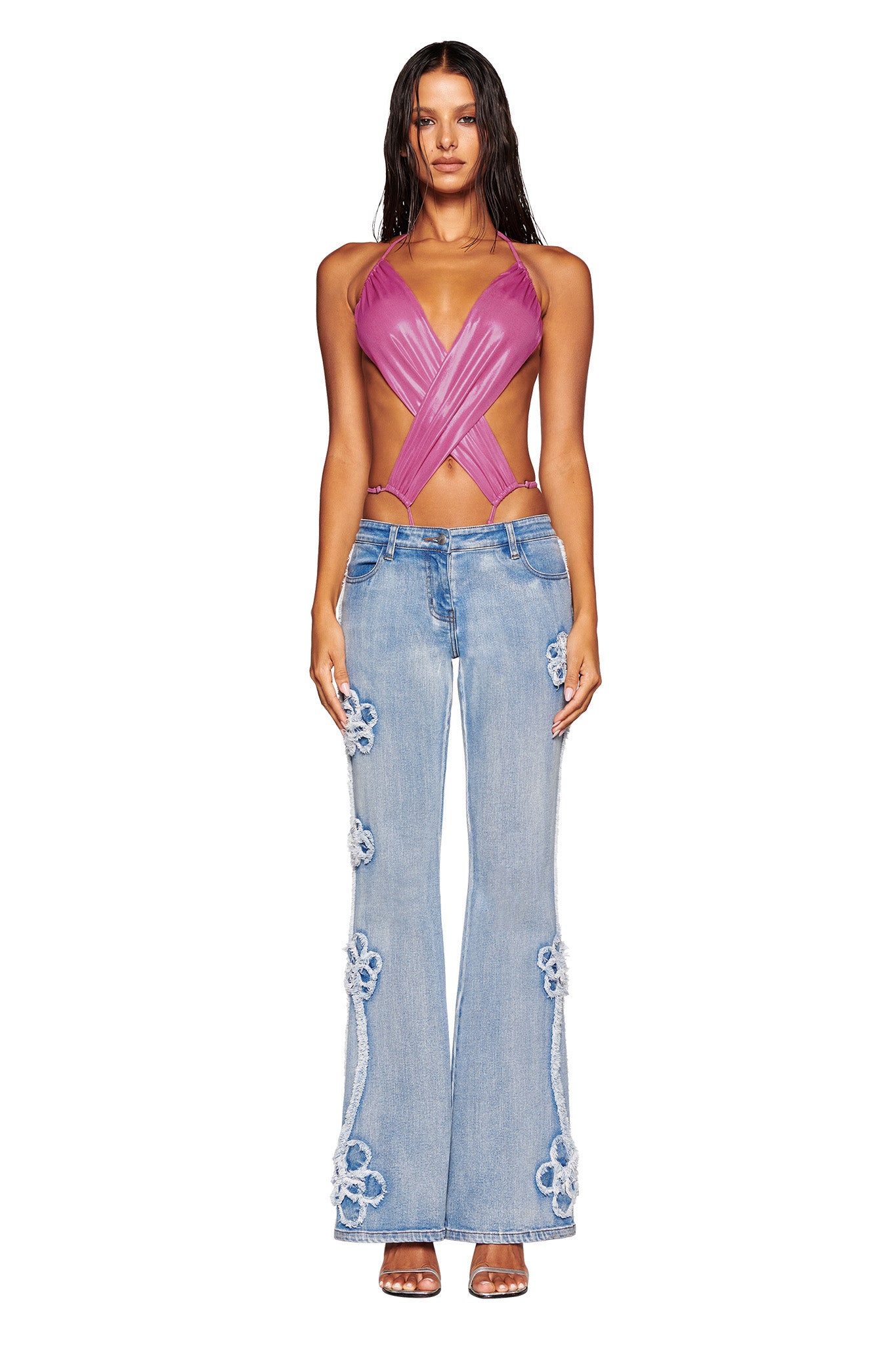 A person stands facing forward, modeling an I.AM.GIA outfit featuring a pink crisscross halter top and the TYLA JEAN - BLUE : DENIM BLUE. The person has long, wet hair and is wearing heeled sandals. The background is plain white.