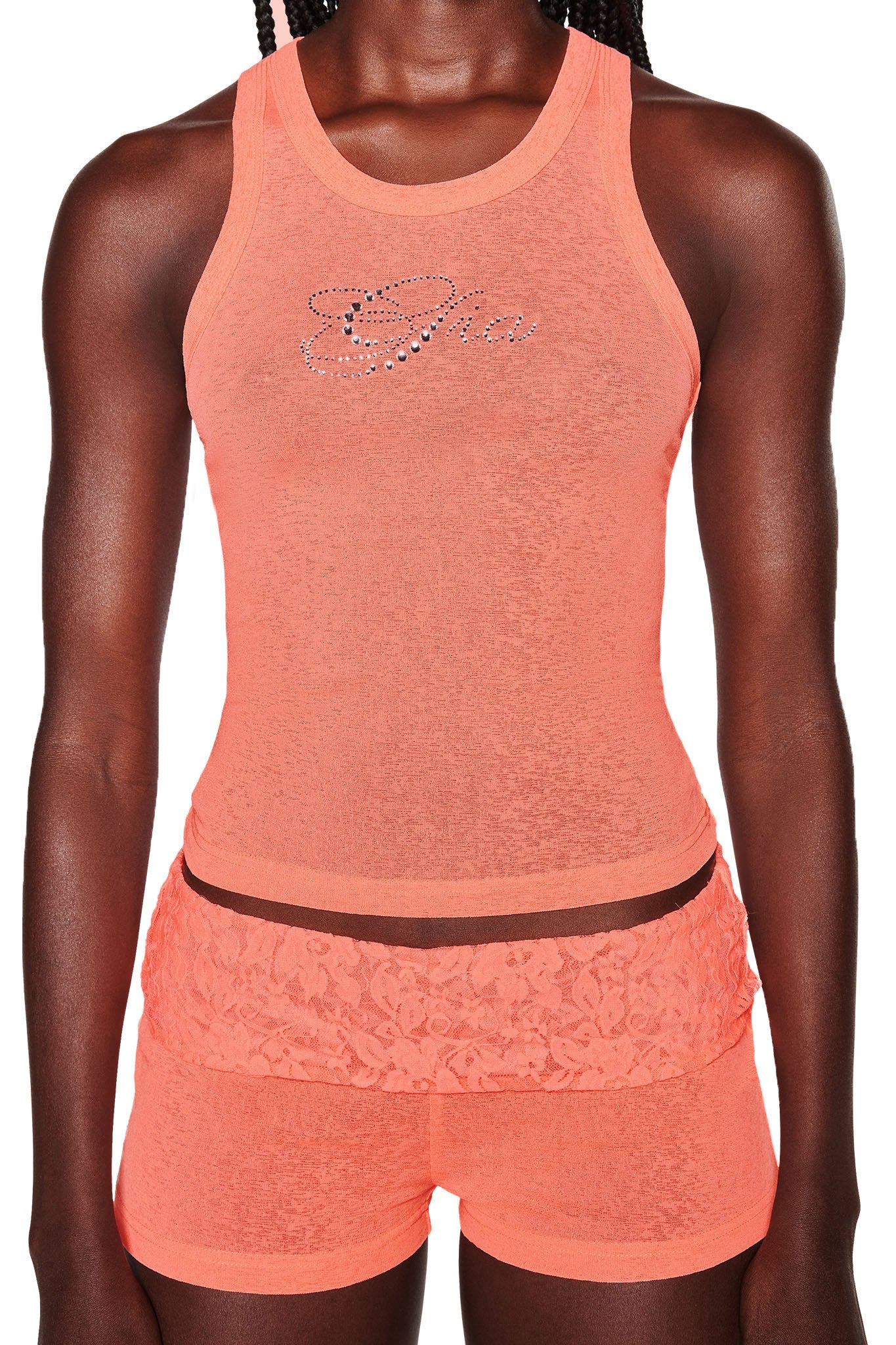 A person is wearing an orange sleeveless top with a decorative design on the chest, paired with I.AM.GIA HURLEY SHORTS in Coral, which feature lace detail around the waist. The outfit appears form-fitting and sporty, with the person's arms resting naturally by their sides.