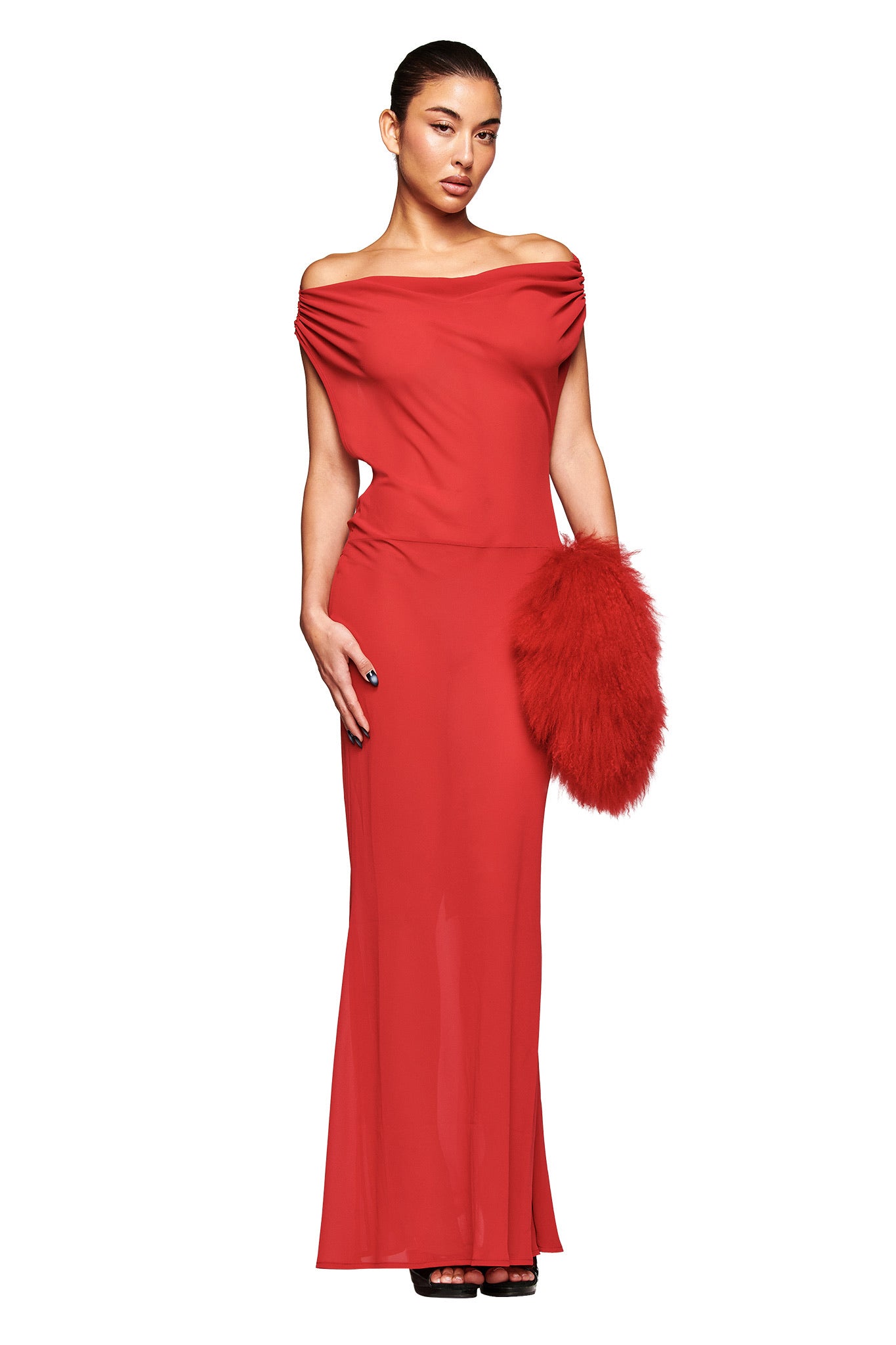 A woman wearing the I.AM.GIA KAHLO MAXI DRESS in red stands against a white background, holding a bold red furry clutch. Sleek hair and black heels finish her sophisticated look.