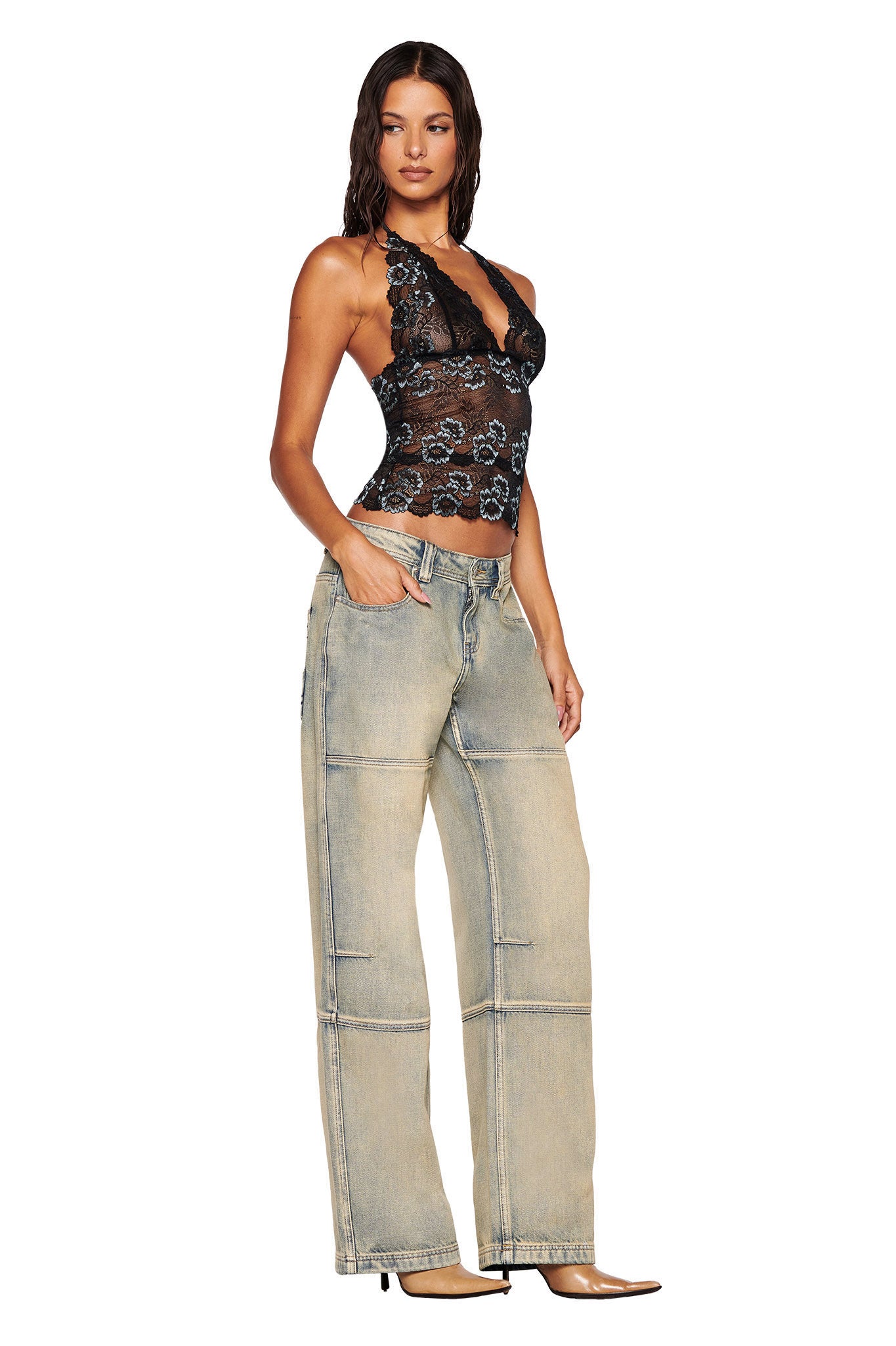 A woman with long dark hair poses in a black lace floral halter top and I.AM.GIA MISTY JEAN - TAN 2.0 light-wash wide-leg, low-rise jeans. She wears pointed-toe heels against a plain white background.