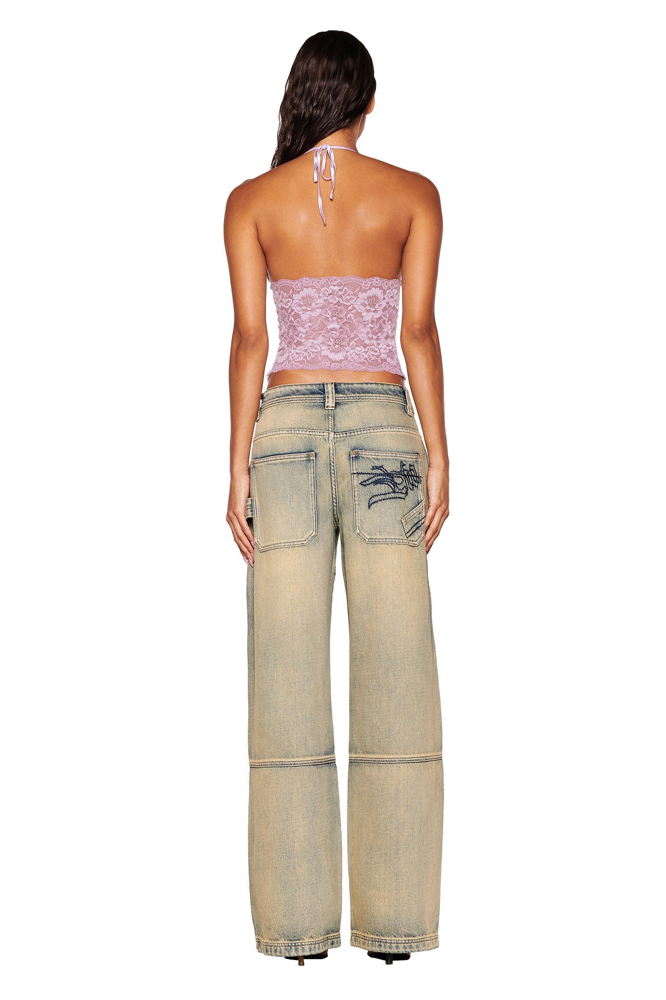 A person with long hair is standing against a plain white background, wearing the GEM HALTER TOP in lilac by I.AM.GIA paired with loose-fitting light blue jeans featuring visible pockets.