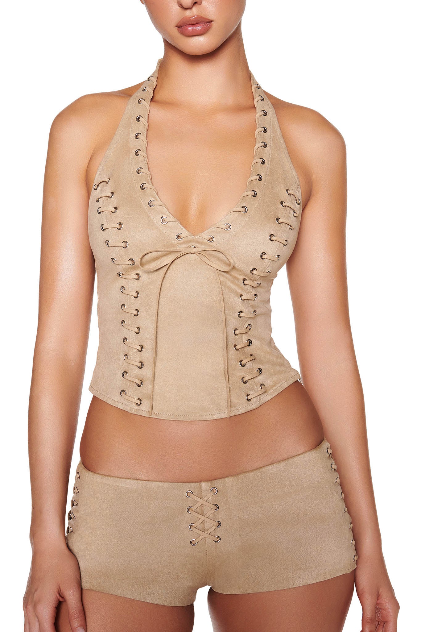 A person showcases I.AM.GIA's RAMONA SHORT in beige and tan. The outfit includes a tan halter top with lace-up details and matching faux suede low-rise hot shorts with a center bow. The person's face is partially obscured.
