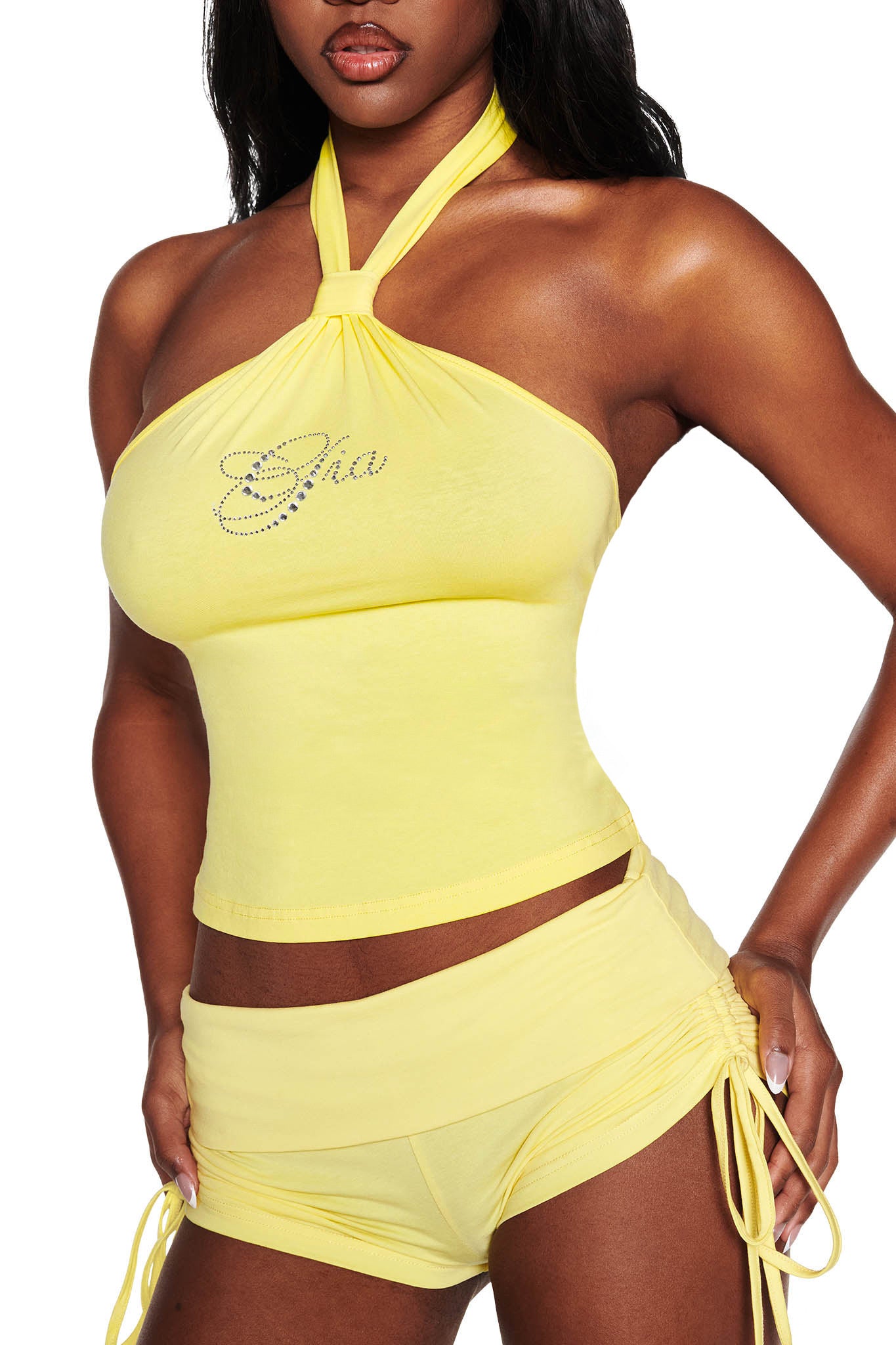 A woman dons a chic, summery outfit from I.AM.GIA: the MIA SHORT - YELLOW, featuring a yellow halter neck top with rhinestone detailing and matching bamboo-fabric low-rise mini shorts with side ties.