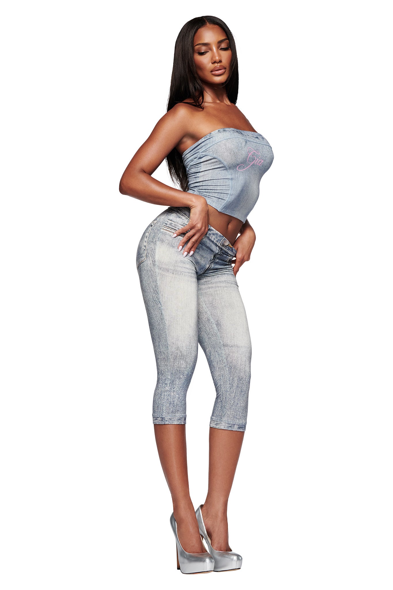 A woman poses in the I.AM.GIA BLARE BOOB TUBE - DENIM TROMPE L’OEIL with matching print leggings and silver heels against a white background.
