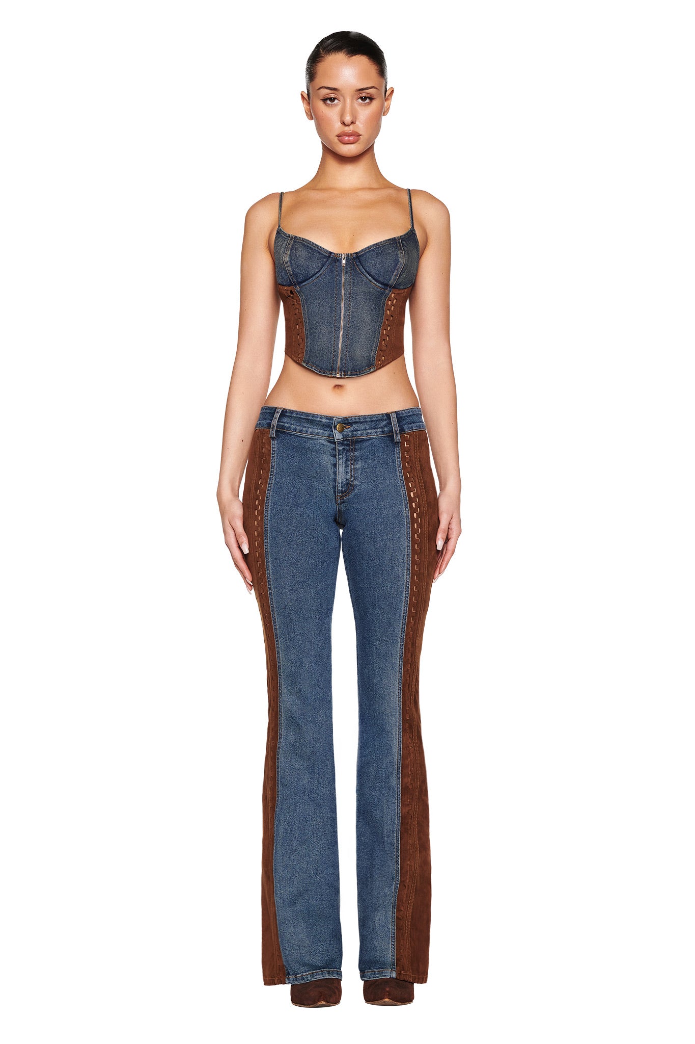 A woman faces forward in I.AM.GIA's FORREST PANT - BLUE: MEDIUM WASH, showcasing the denim corset top and mid-rise flare jeans with brown suede panels and decorative stitching. Her hair is tied back against a plain white background, highlighting her stylish outfit's vintage washed effect.