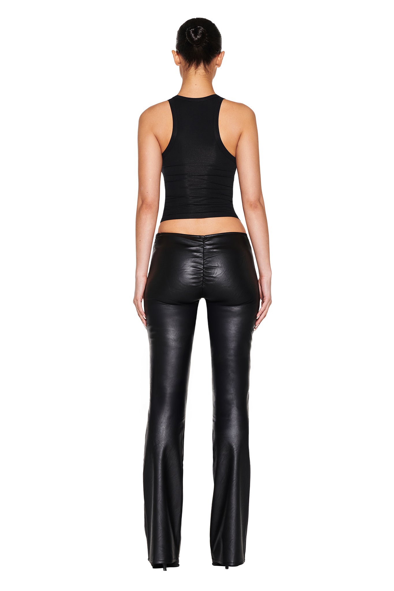 With their back to the camera, this person wears I.AM.GIA's ARIES ZODIAC TANK in black and bodycon leather pants with flared legs. Their hair is styled in a bun against a crisp white background.
