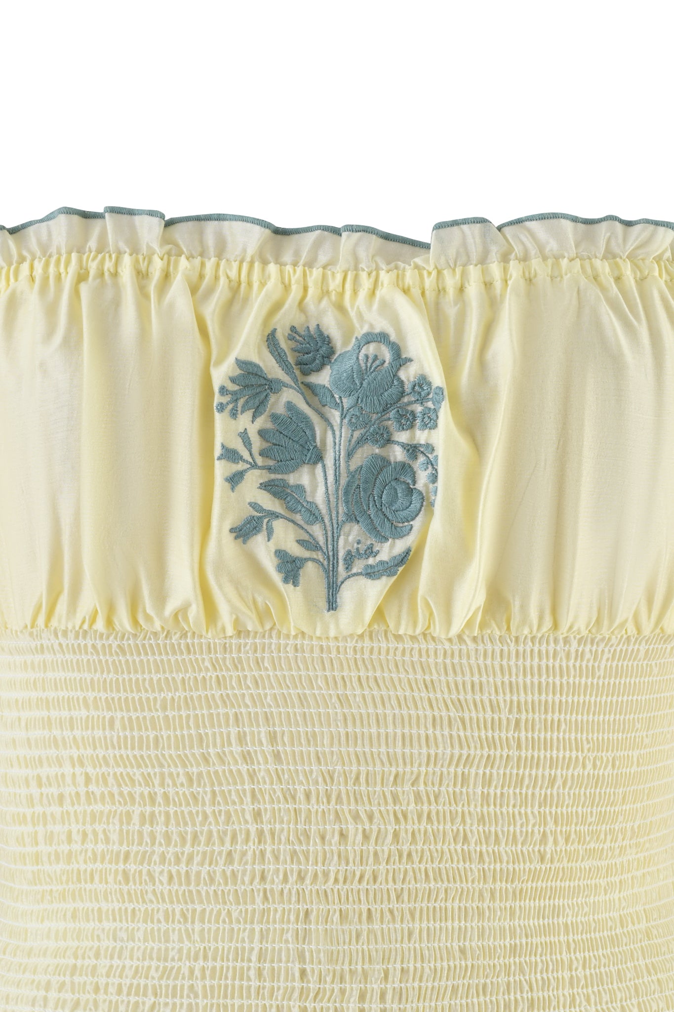 Close-up of the CLOVER TOP - YELLOW by I.AM.GIA, featuring pale yellow smocked fabric with shirring details, a ruffled trim on the top edge, and central blue floral embroidery of delicate leaves and blossoms.