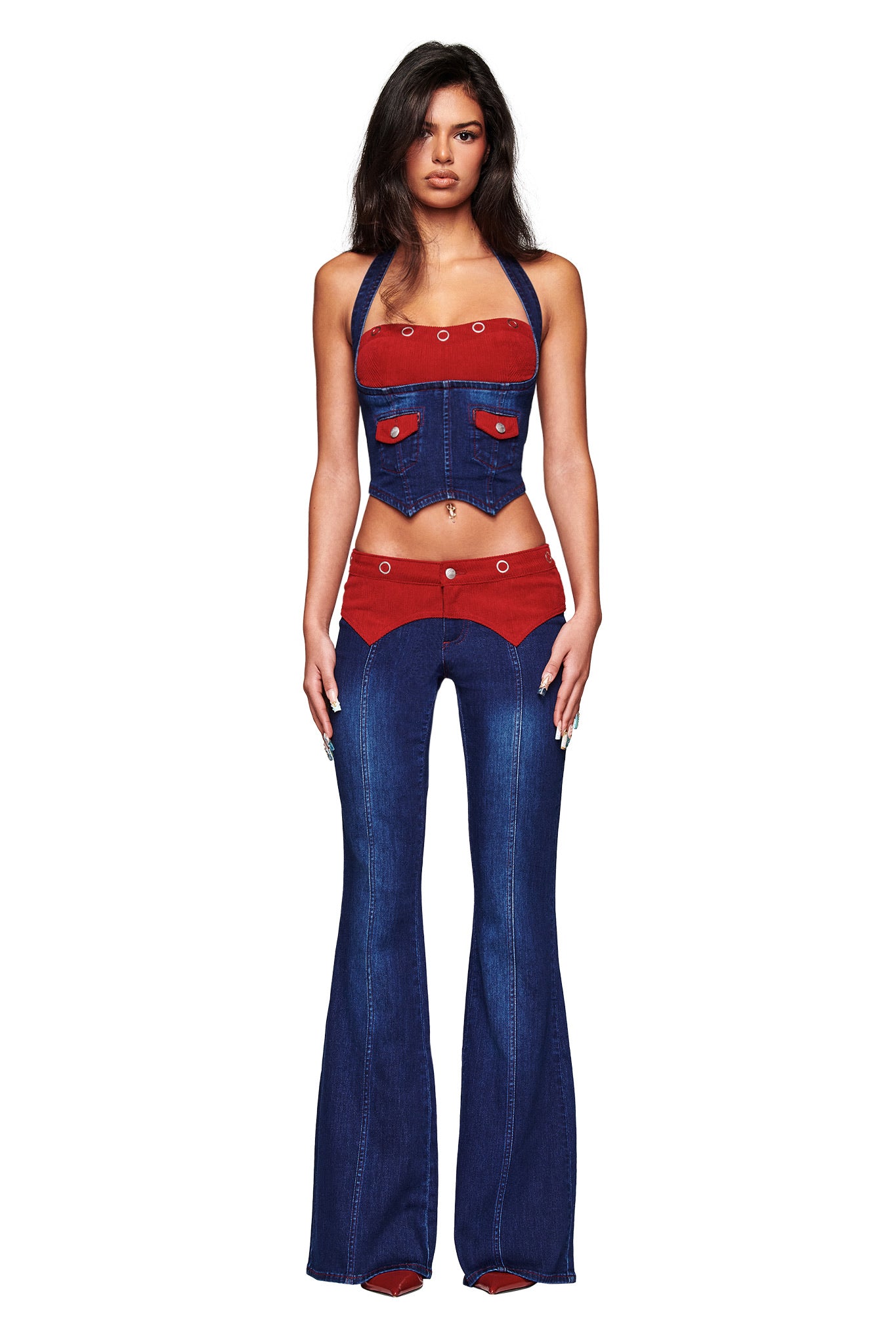 A woman faces forward wearing the I.AM.GIA TOMMIE CORSET - DARK WASH RUBY, a halter neck denim top with a red corduroy bust, paired with flared jeans featuring red accents and button details, set against a plain white background.