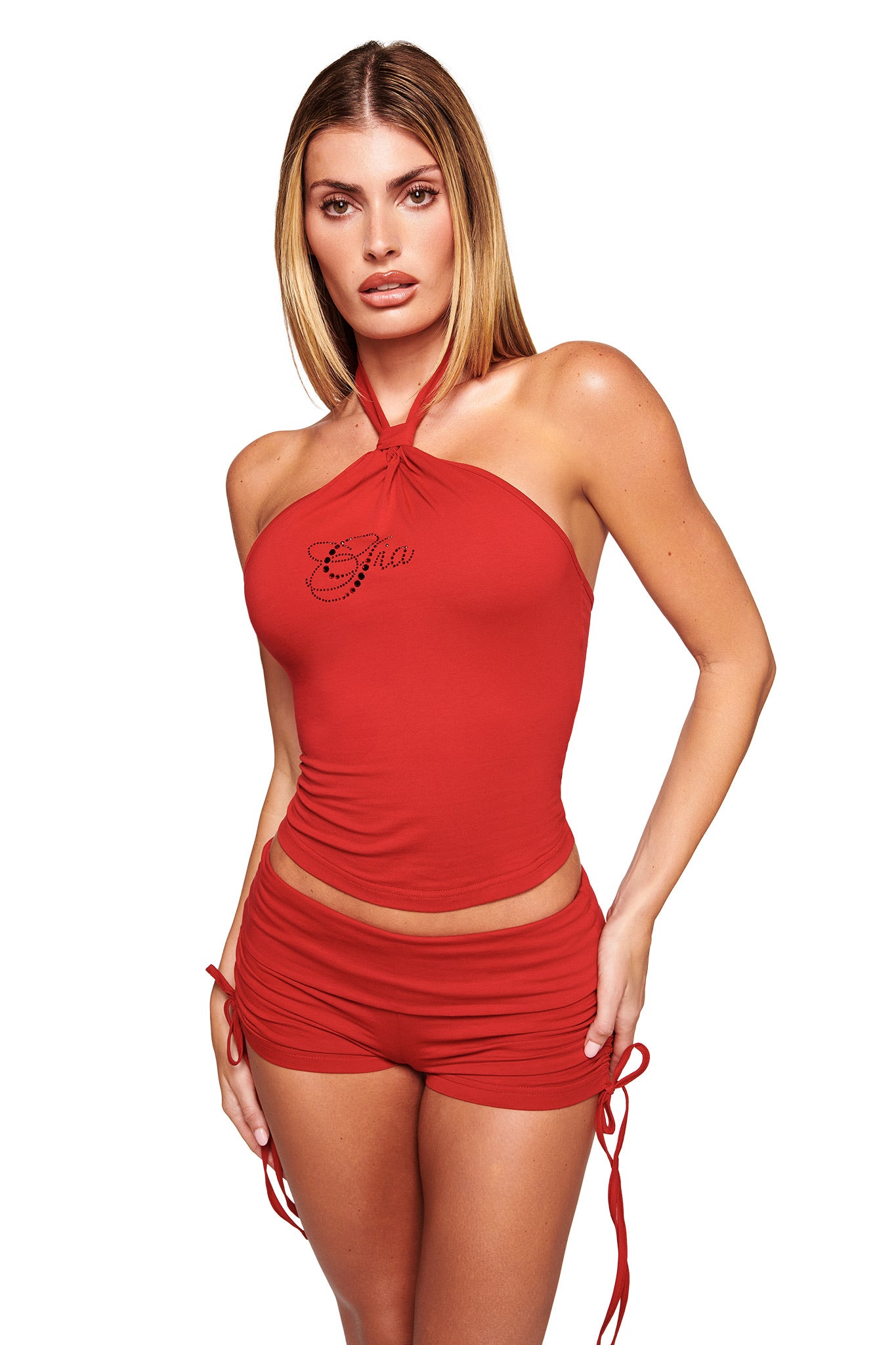 A woman with straight, light brown hair wears the I.AM.GIA ROWAN TOP in rich red, a bodycon halter style with "Chic" text, paired with matching red ruched shorts, standing against a plain white background.