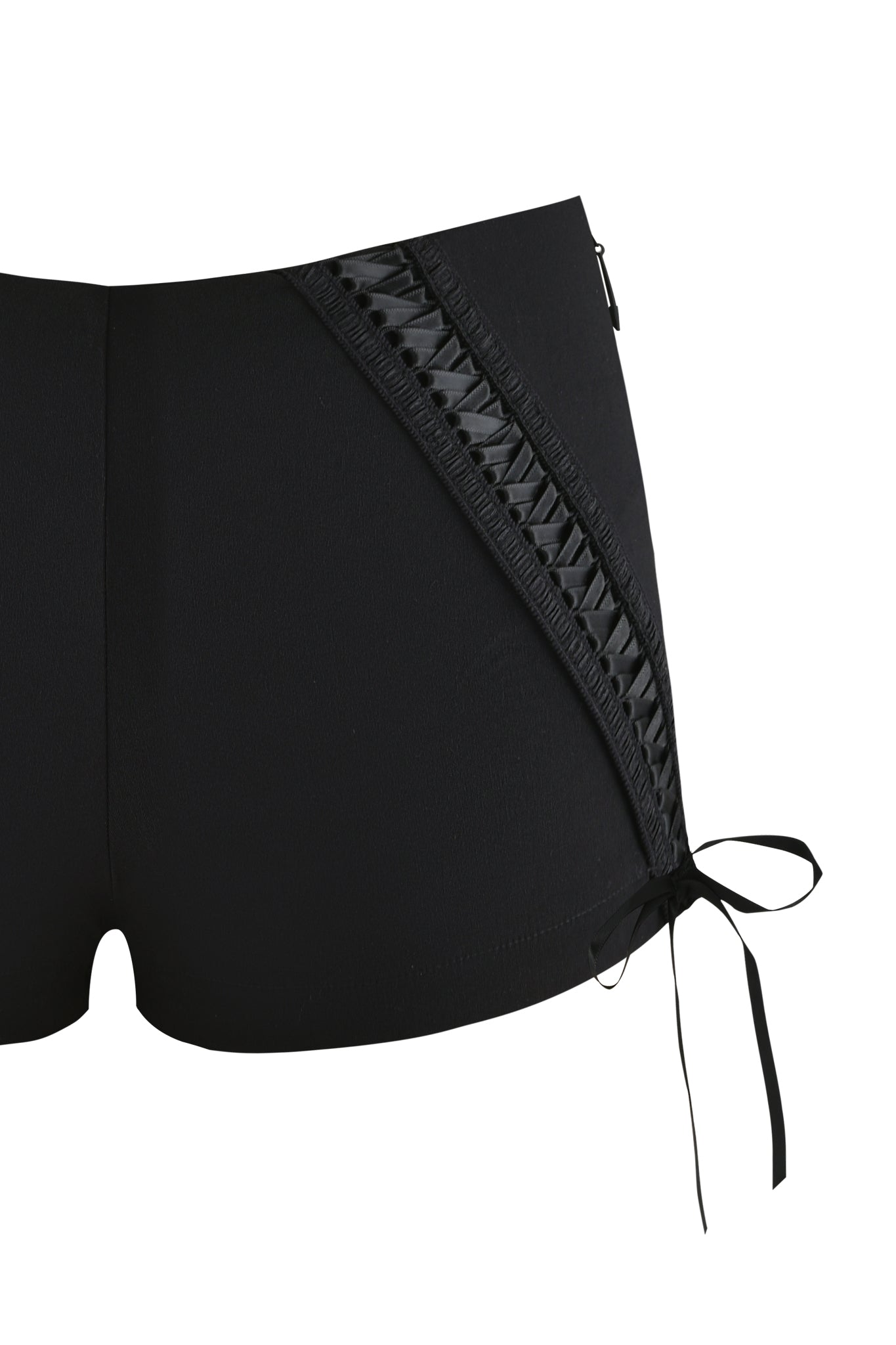 The SAMIRA SHORT - BLACK by I.AM.GIA is a black lace-up hot short with a bodycon fit, featuring crisscross ribbon and eyelets on the left side, finished with a bow at the hem. Only the midsection and upper legs are visible.
