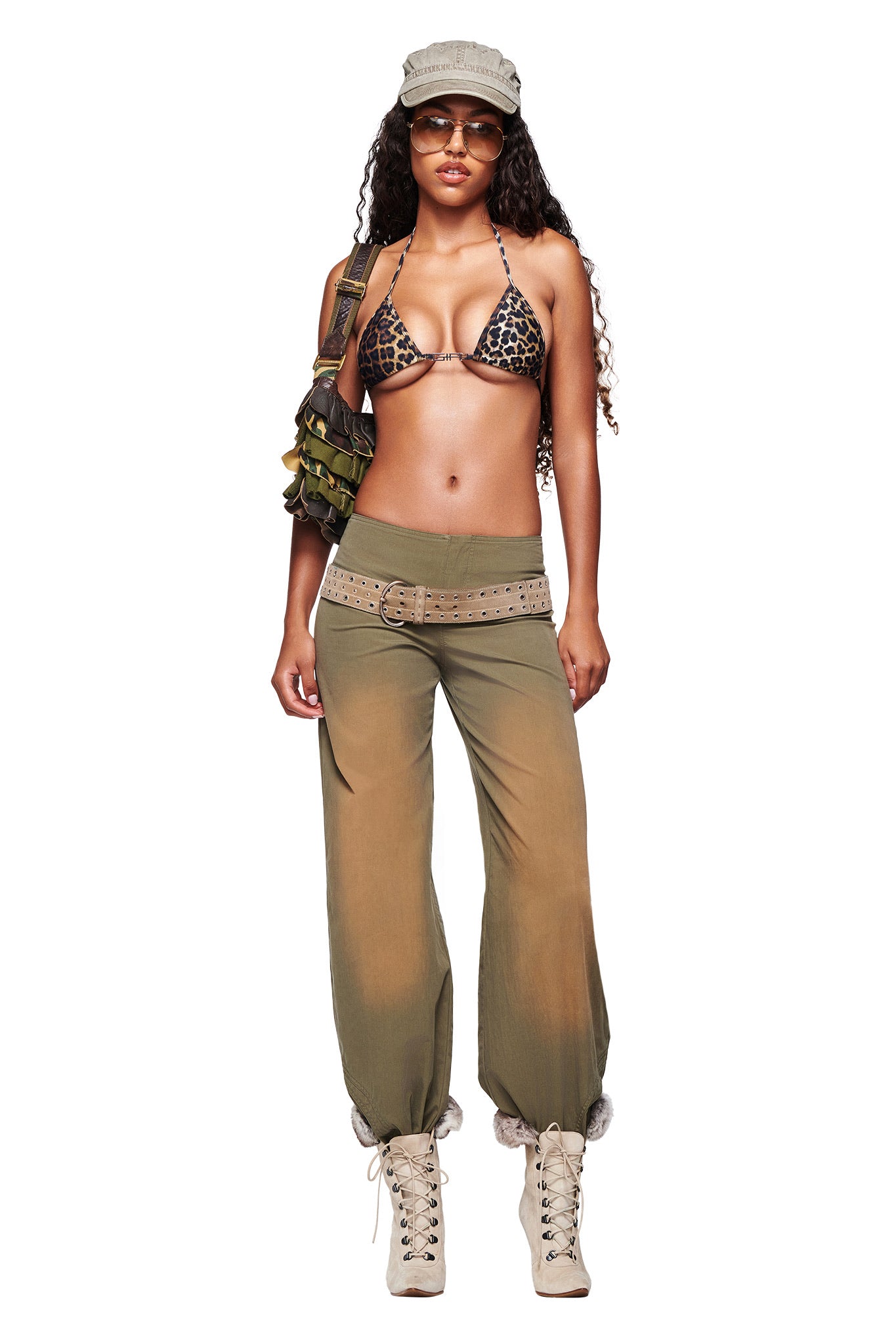 A woman wears I.AM.GIA SEQUOIA PANT in army green with a leopard print bikini top, beige lace-up boots, a wide belt, military-style cap, sunglasses, and a camo bag, standing against a white background.