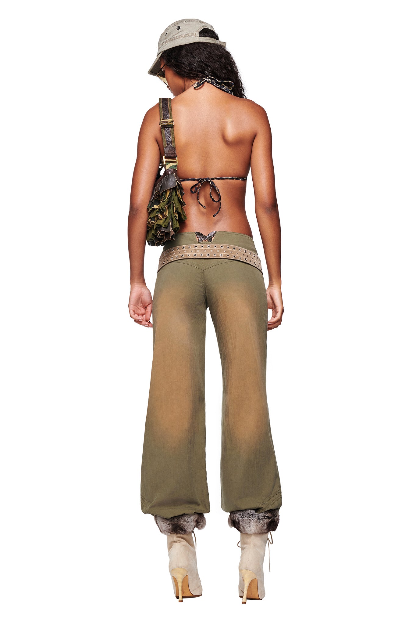 A woman with long hair, seen from behind, wears a bucket hat, bikini top, boots, a shoulder bag, and I.AM.GIA SEQUOIA PANT in army green. A butterfly tattoo is visible on her lower back.