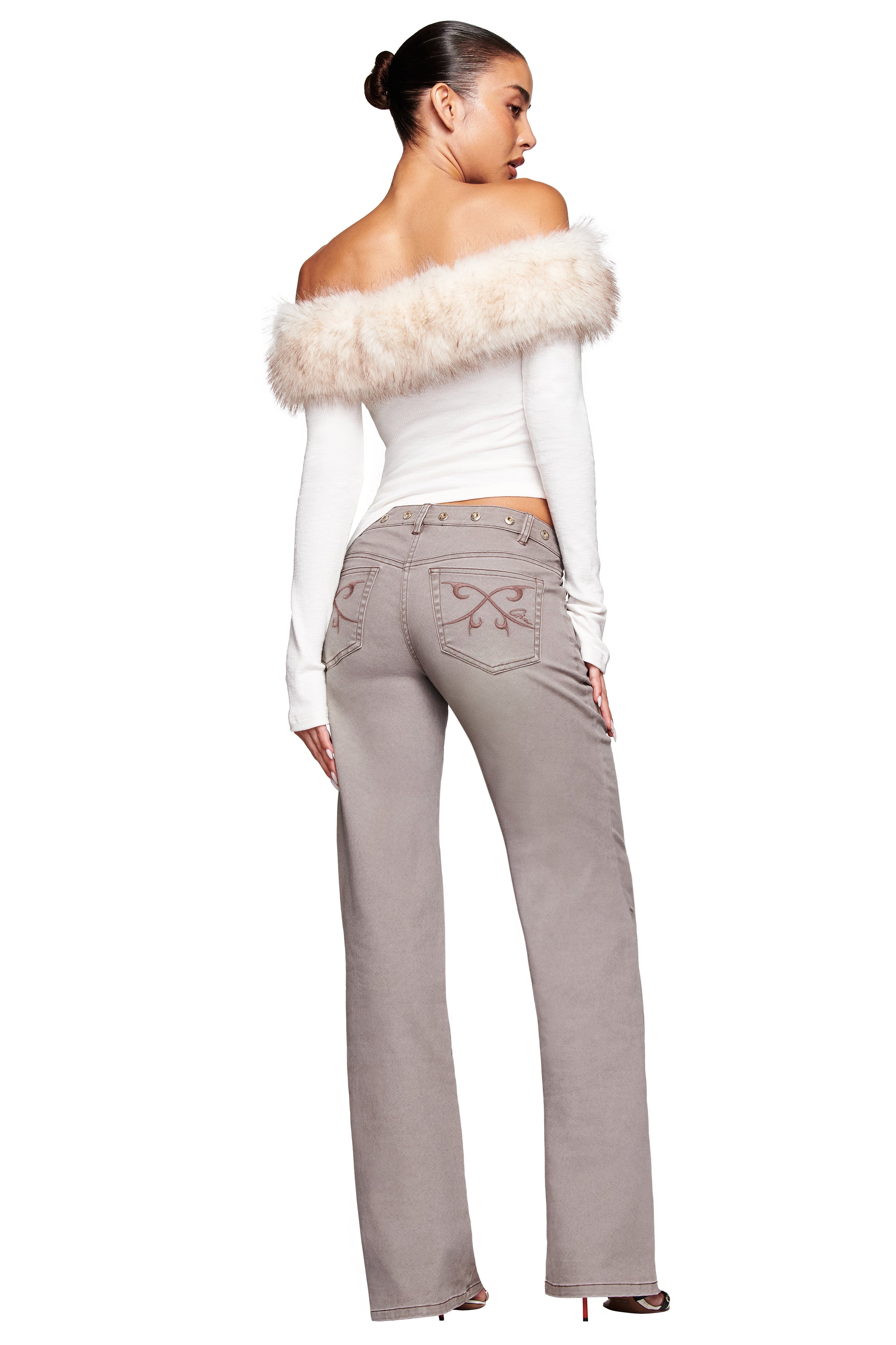 A woman faces away in a white off-the-shoulder top with faux fur trim and I.AM.GIA GREER PANT in grey, featuring butterfly embroidery. Her hair is in a bun, she wears heeled shoes, against a white background.