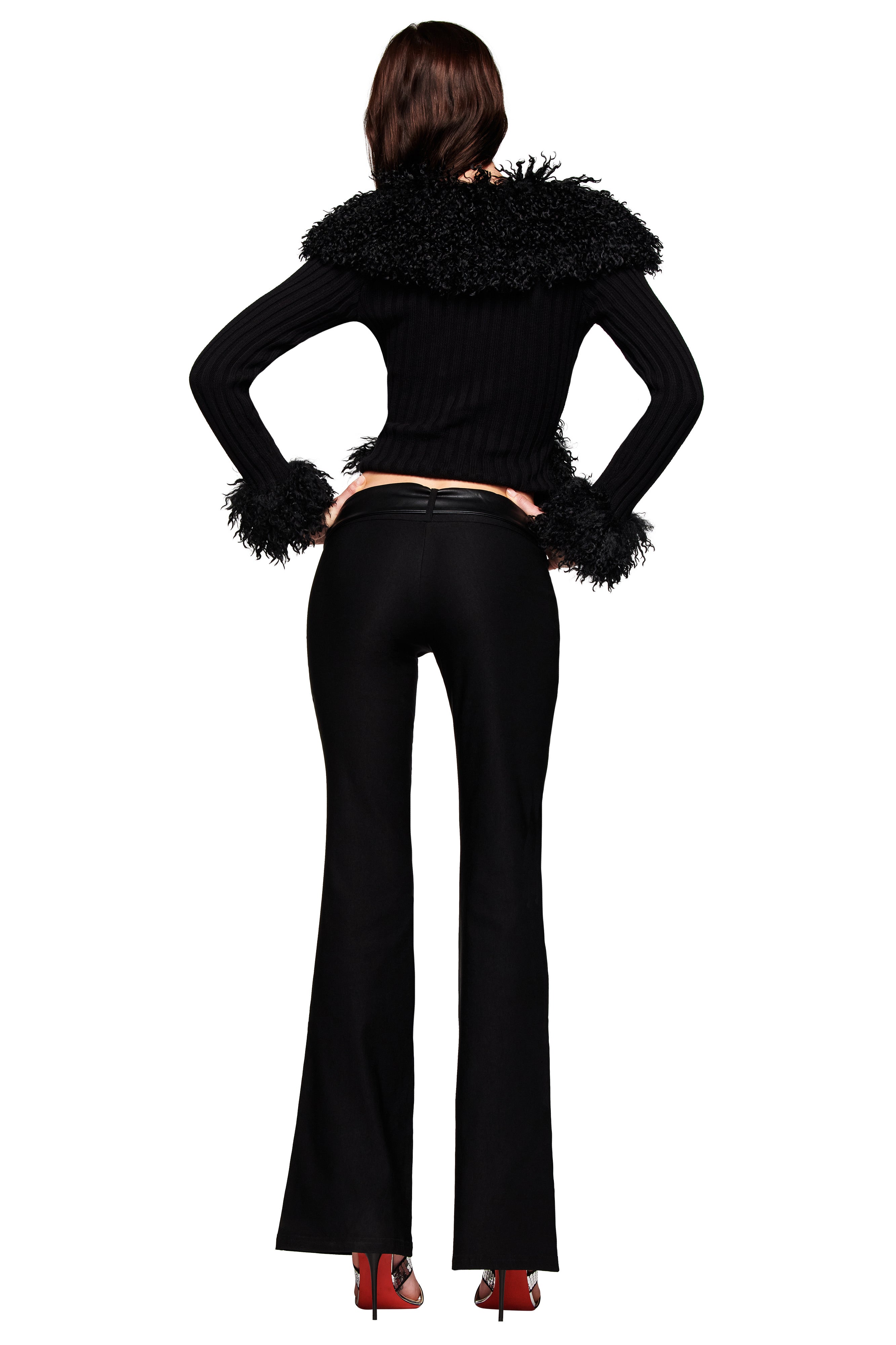 A person faces away, wearing the I.AM.GIA CRESSIDA JACKET in black with textured trim on the shoulders and cuffs, paired with black flared pants and red high heels.