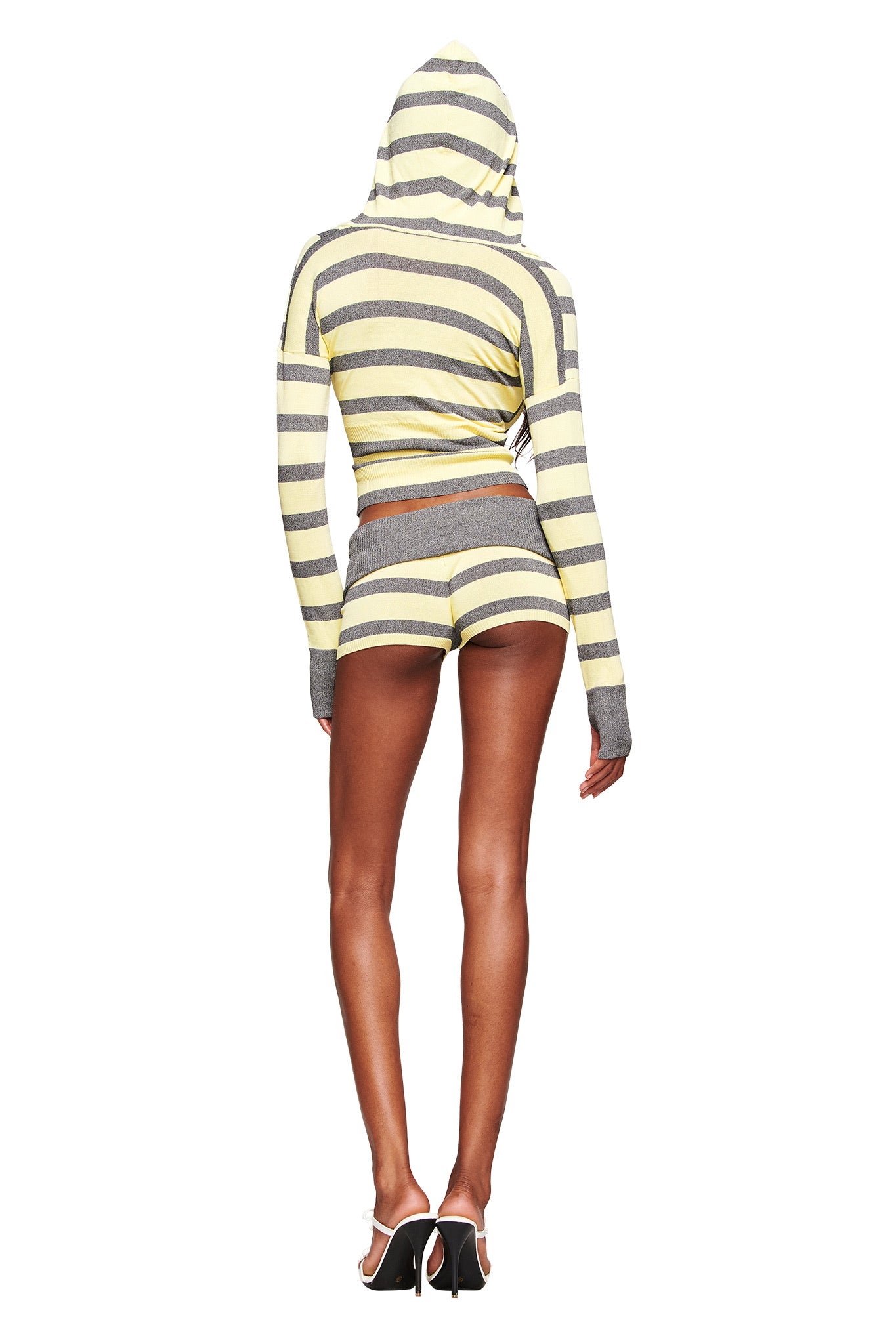 A person stands facing away, wearing the I.AM.GIA SUZI SHORT - YELLOW AND GREY STRIPE micro mini shorts with an adjustable waistband and a matching hoodie, paired with white high-heeled shoes against a white background.