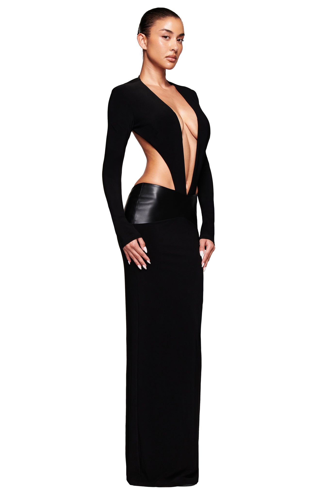 A woman poses against a plain white background wearing the I.AM.GIA CARMINA MAXI DRESS in black, a slinky, bodycon style with long sleeves, dramatic side and torso cutouts, and a deep plunging neckline.