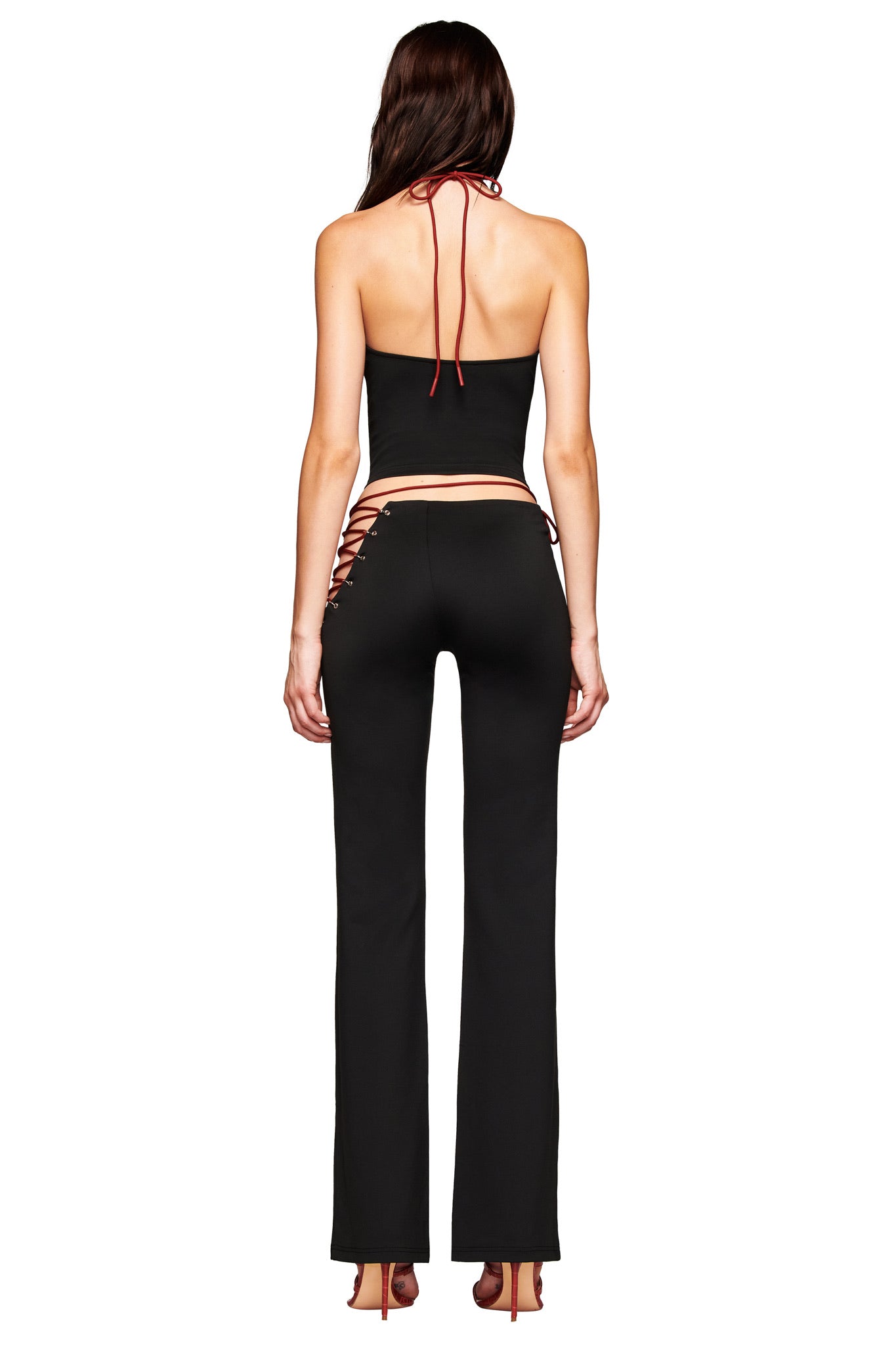 A woman wearing the I.AM.GIA ONYX PANT in black, featuring a low-rise fit and eyelet details, paired with a matching top.