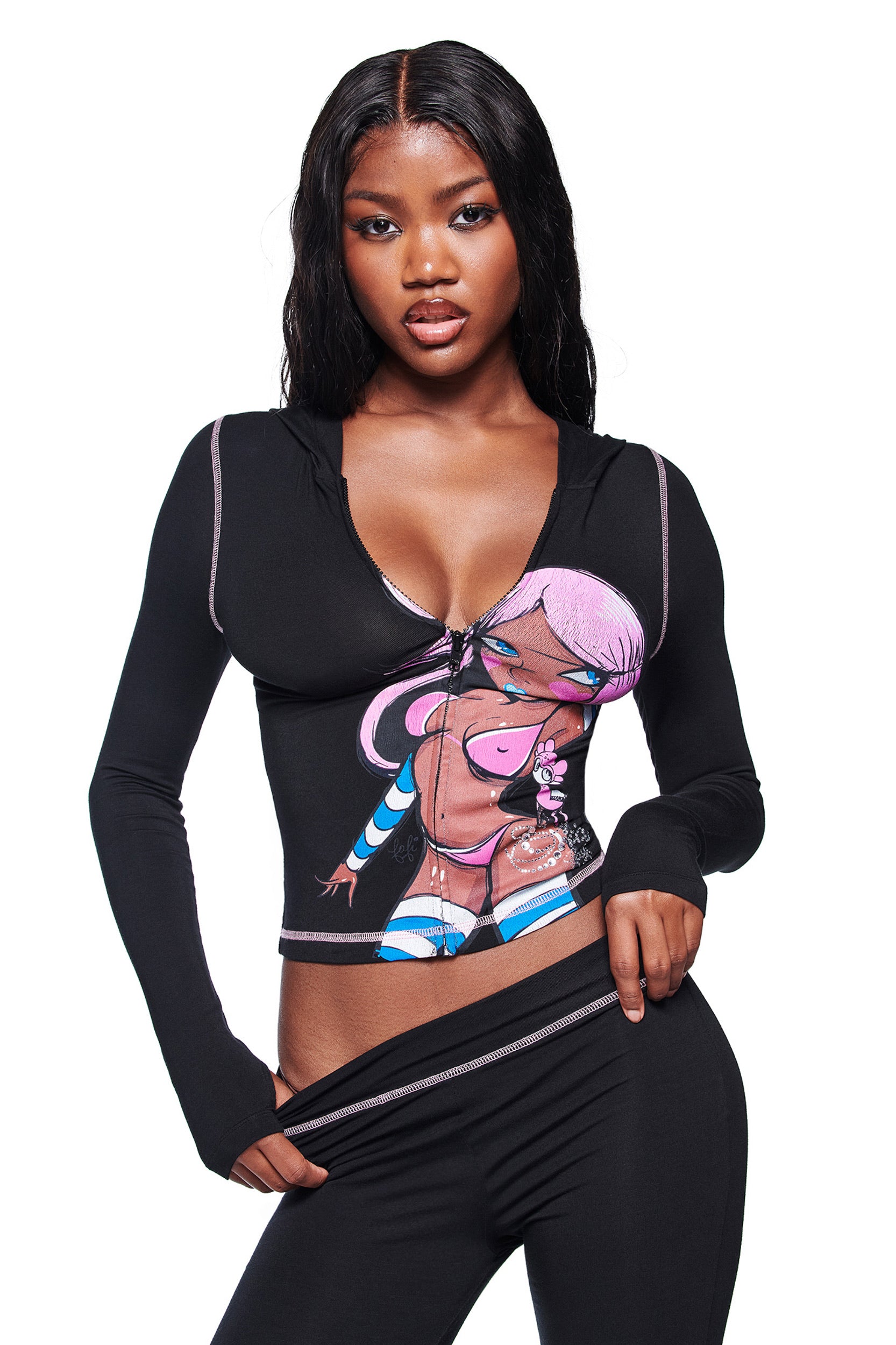A woman with long dark hair, wearing the I.AM.GIA FAFI BLARE HOODIE in black featuring a cartoon graphic, and matching black pants, poses against a white background.