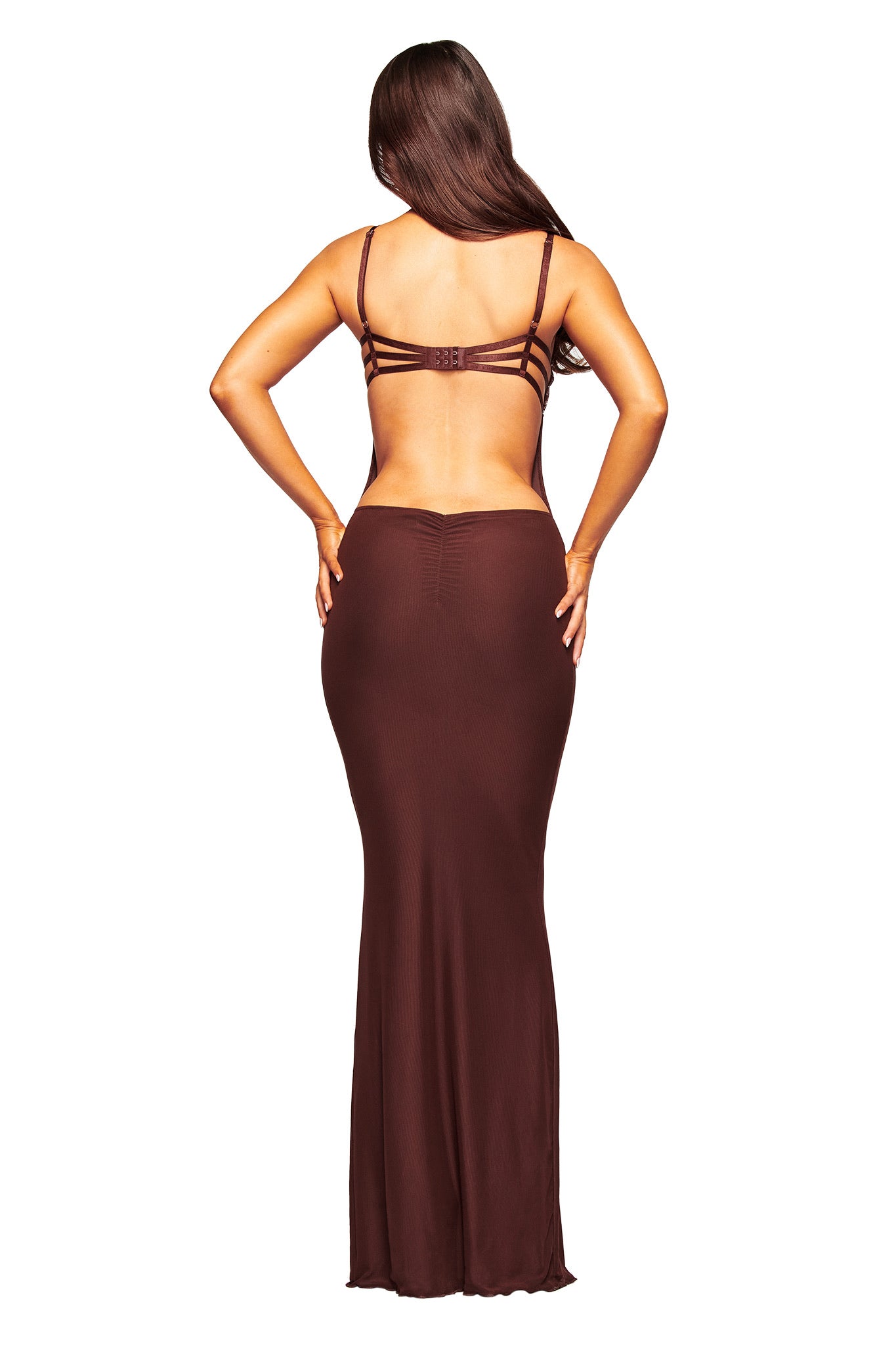 A woman faces away, wearing the I.AM.GIA SILO MAXI DRESS in brown. The dress features thin straps and a long, fitted skirt as her long hair falls down her back and her hands rest on her hips.
