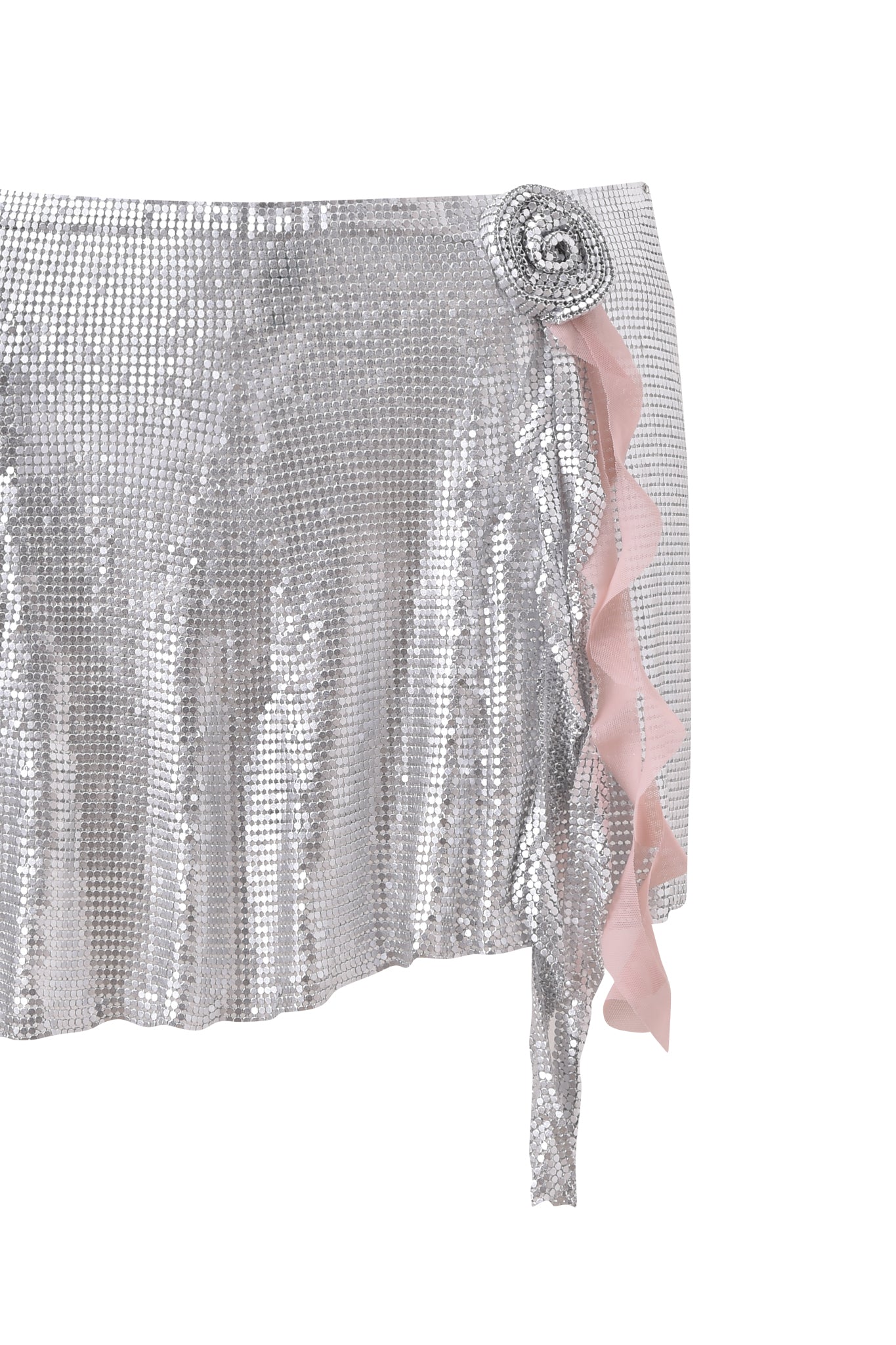 The MILANA MINI SKIRT - SILVER by I.AM.GIA is a shiny chainmail mini skirt with a textured grid pattern, featuring a pink ruffle detail and a circular waist embellishment.