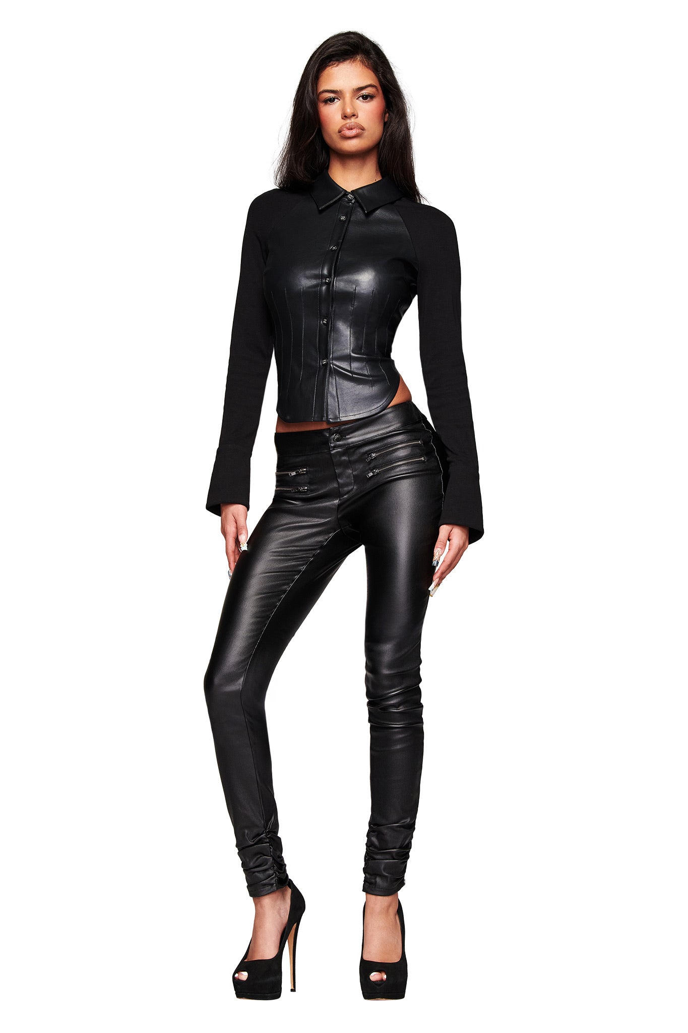 A woman models the I.AM.GIA JETT PANT - BLACK, a fitted waxed faux leather skinny pant with zipper details, paired with black heels against a white background.