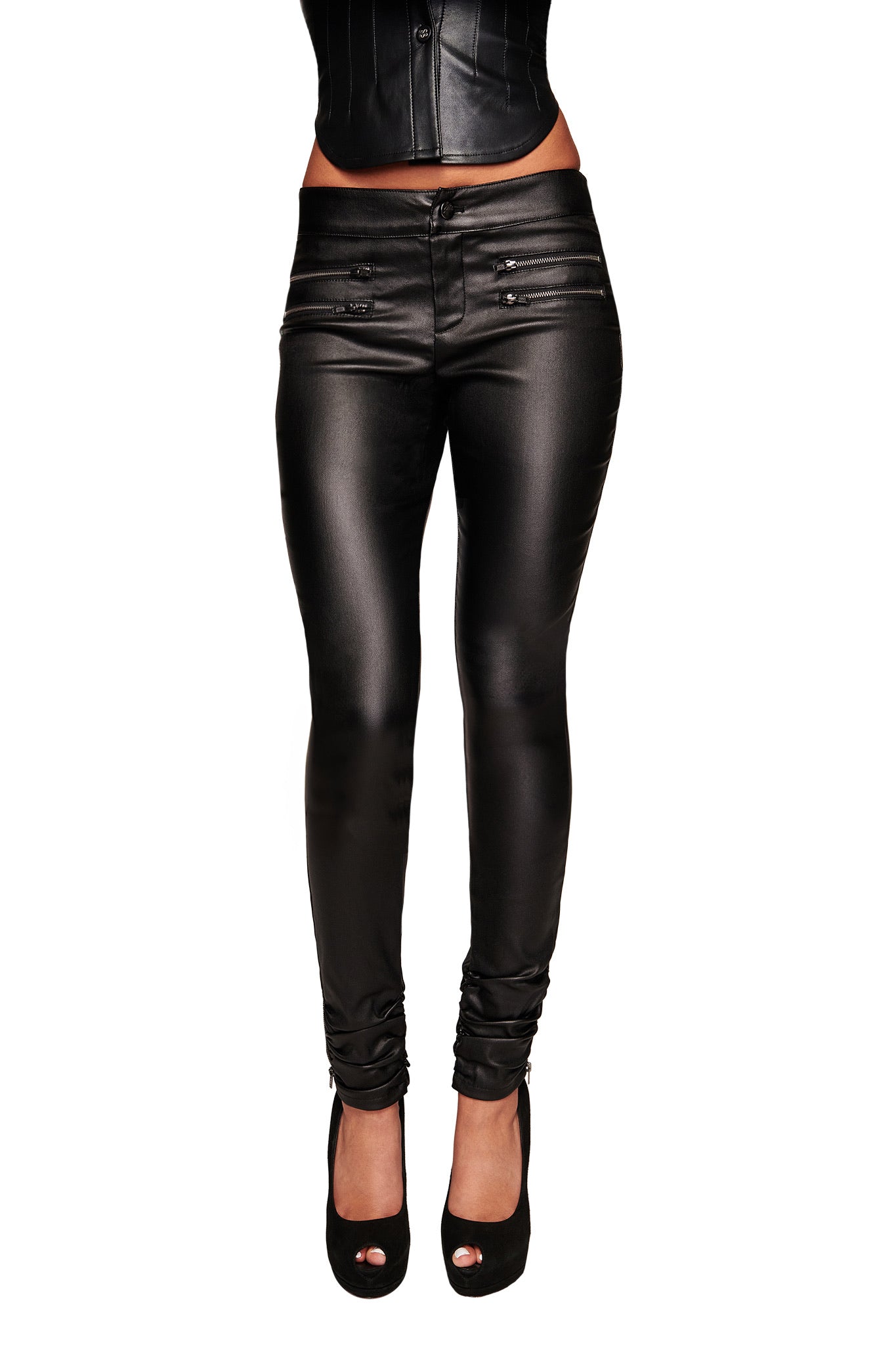 A person wearing I.AM.GIA JETT PANT - BLACK skinny jeans with a waxed finish, paired with a black corset-style top and black open-toe heels, shown from waist to feet against a white background.