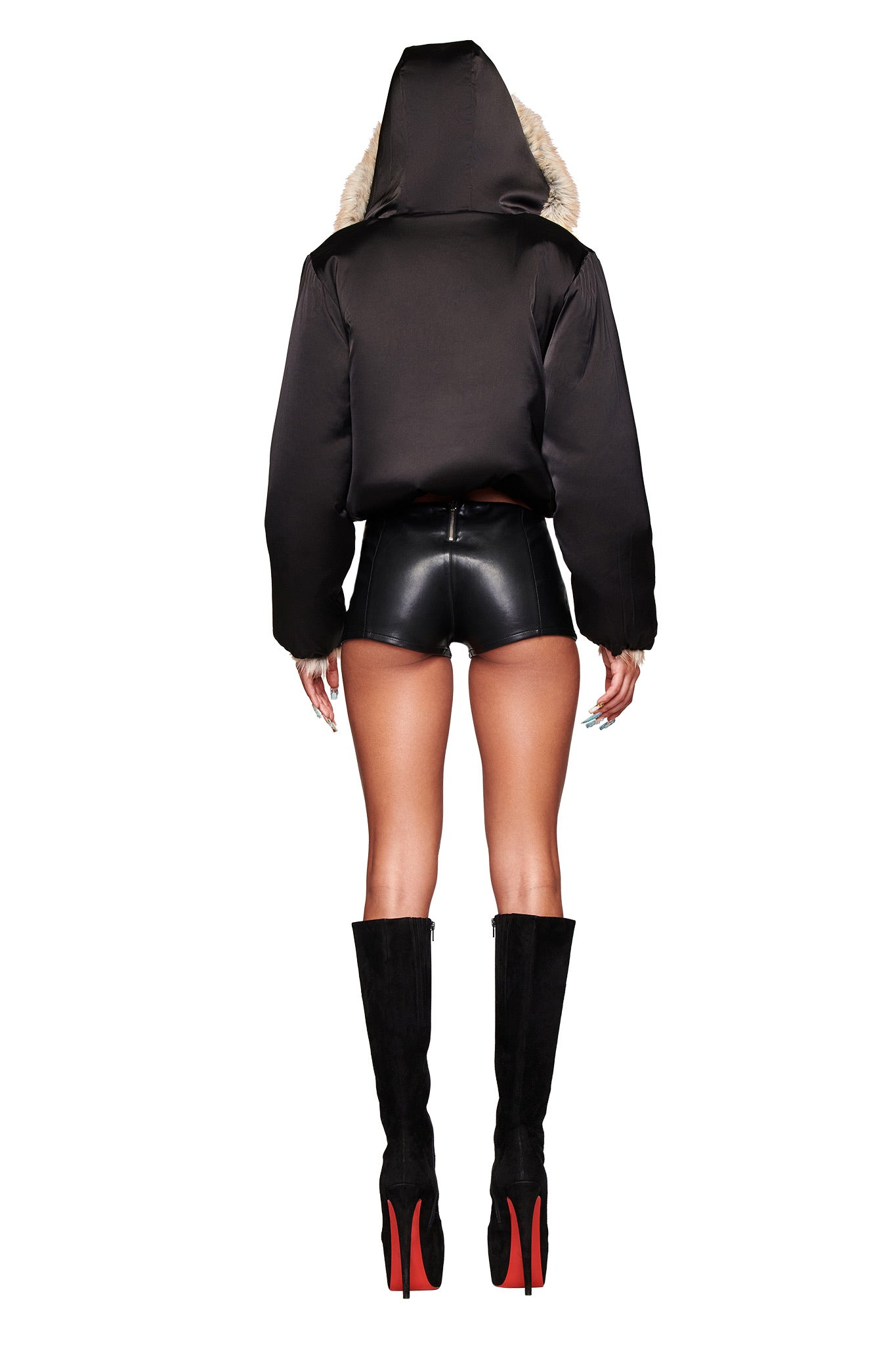 A person faces away, wearing the I.AM.GIA EVEREST REVERSIBLE JACKET in brown with faux fur trim, paired with black leather shorts and knee-high black boots with red soles, set against a white background.