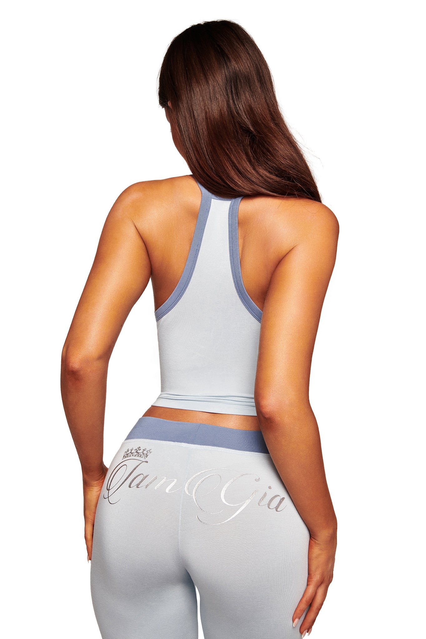 A woman with long brown hair is seen from behind wearing a light blue athletic outfit, featuring a racerback top and I.AM.GIA's BLARE LOWER RISE TRACKPANT - TWO TONE POWDER BLUE with the brand name on the back.
