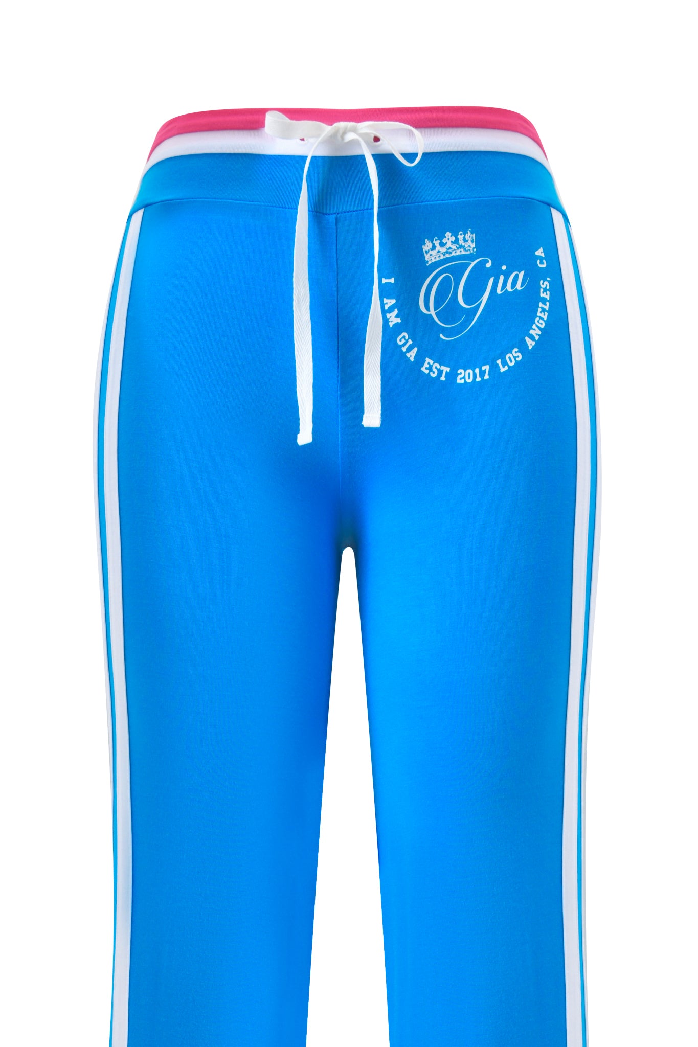 The BLARE STRIPED TRACKPANT by I.AM.GIA features a sky blue color with white side stripes, a pink waistband, and a white drawstring. A small crown tops the I.AM.GIA "Gia EST 2017 LOS ANGELES, CA" logo on the left hip. Straight leg design.