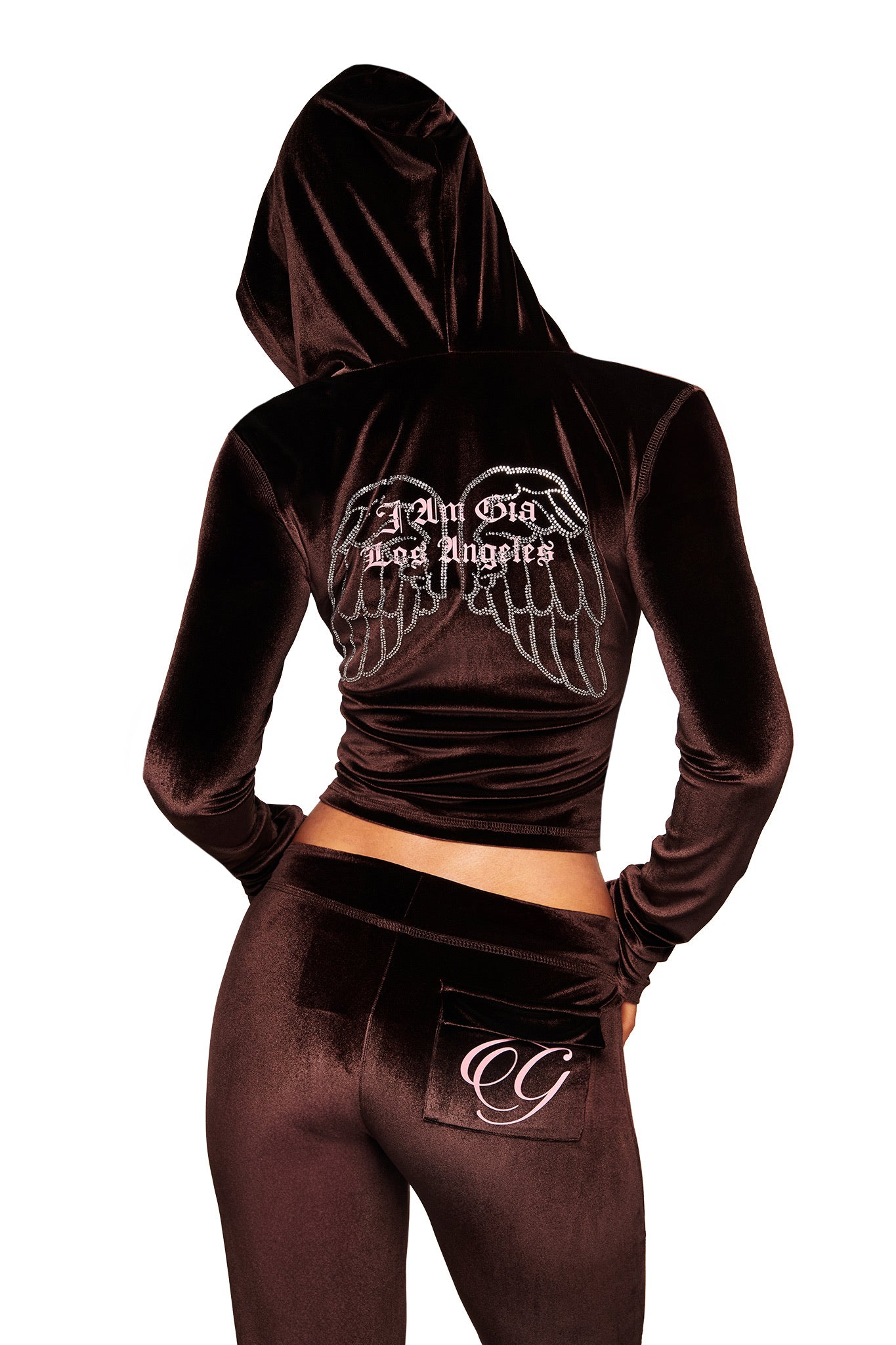 Someone wears the I.AM.GIA BLARE VELOUR POCKET HOODIE in chocolate, hood up. The back shows diamanté angel wings and "All Glad Los Angeles" text. The pants have a pocket detailed with a decorative GIA script logo.