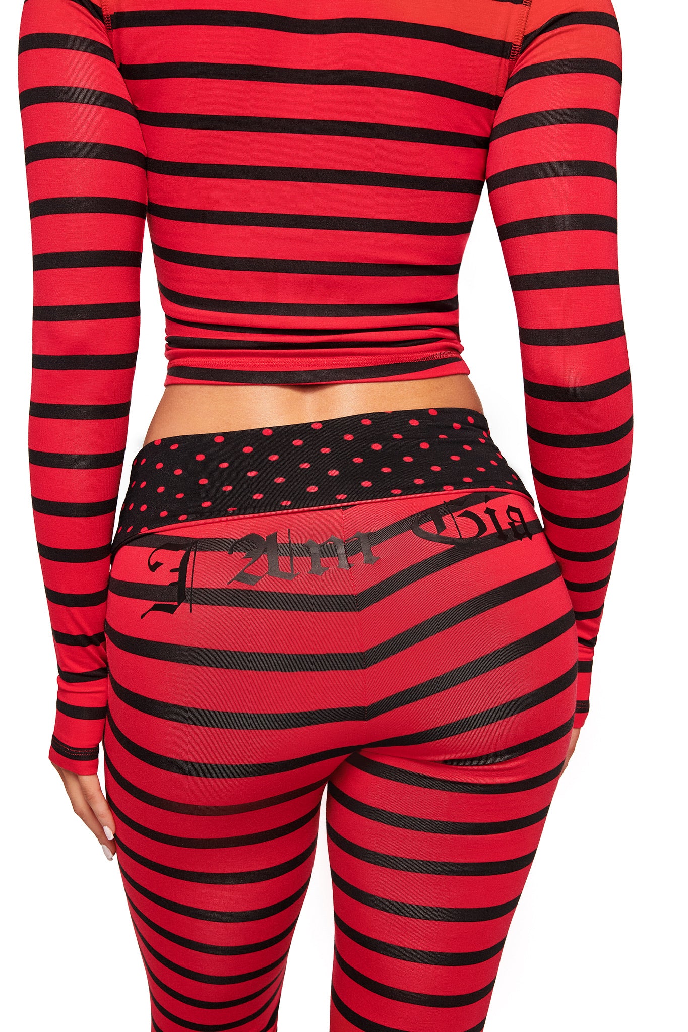 A person shown from the back wearing I.AM.GIA's BLARE FOLDOVER TRACKPANT in red and black stripe, paired with a matching crop top featuring a foldover waistband, black polka dots, and printed text.