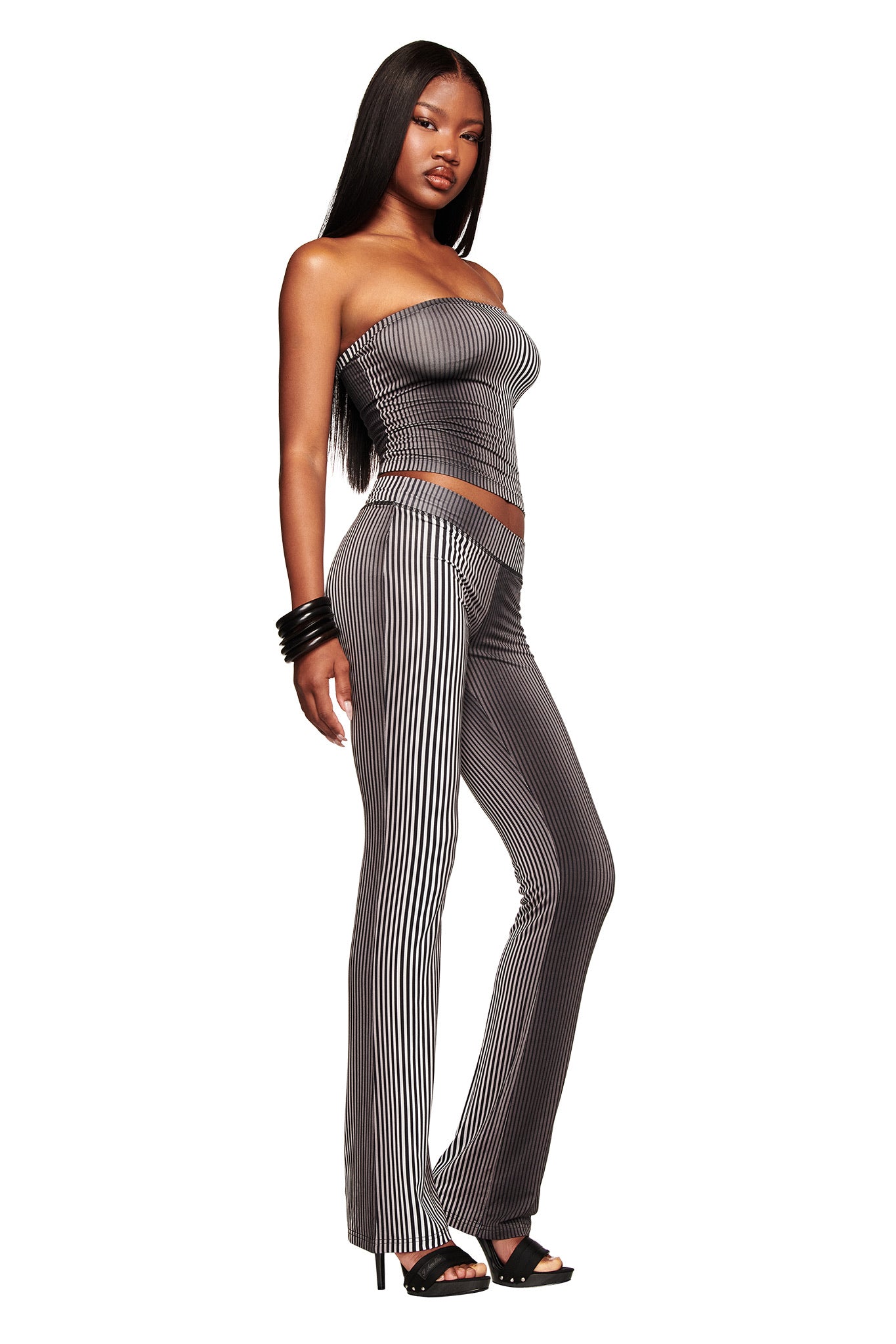 A woman poses confidently against a white background in the I.AM.GIA TRINITY 2-IN-1 SKIRT PANT - STRIPE with a matching strapless top, black heels, black bracelets, and long straight hair.