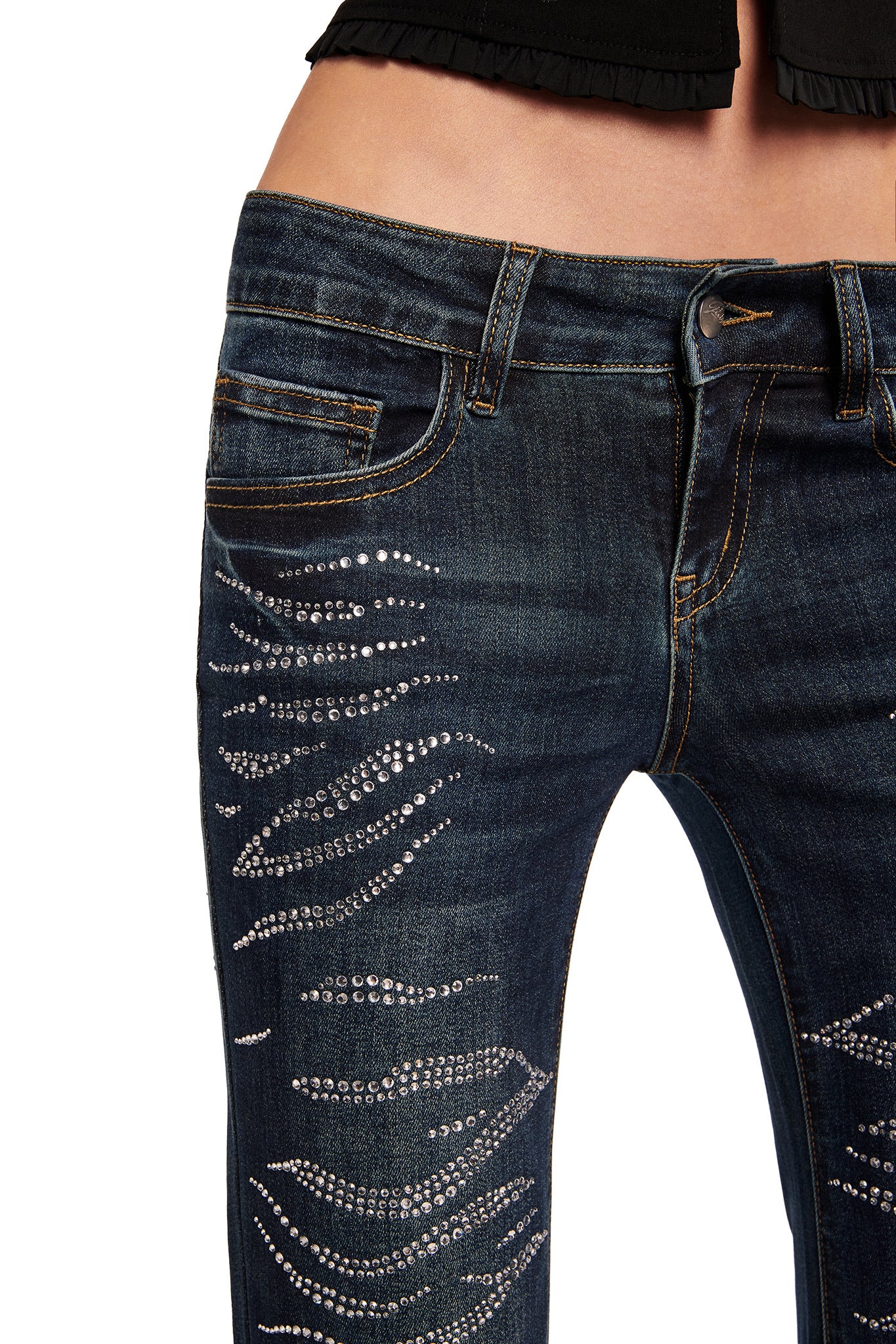 Close-up of a person wearing I.AM.GIA's JIJI DIAMONTE JEAN - BLUE, featuring low rise bootcut denim with rhinestone embellishments on the thighs and legs, classic pockets, button-zip closure, styled with a black top.