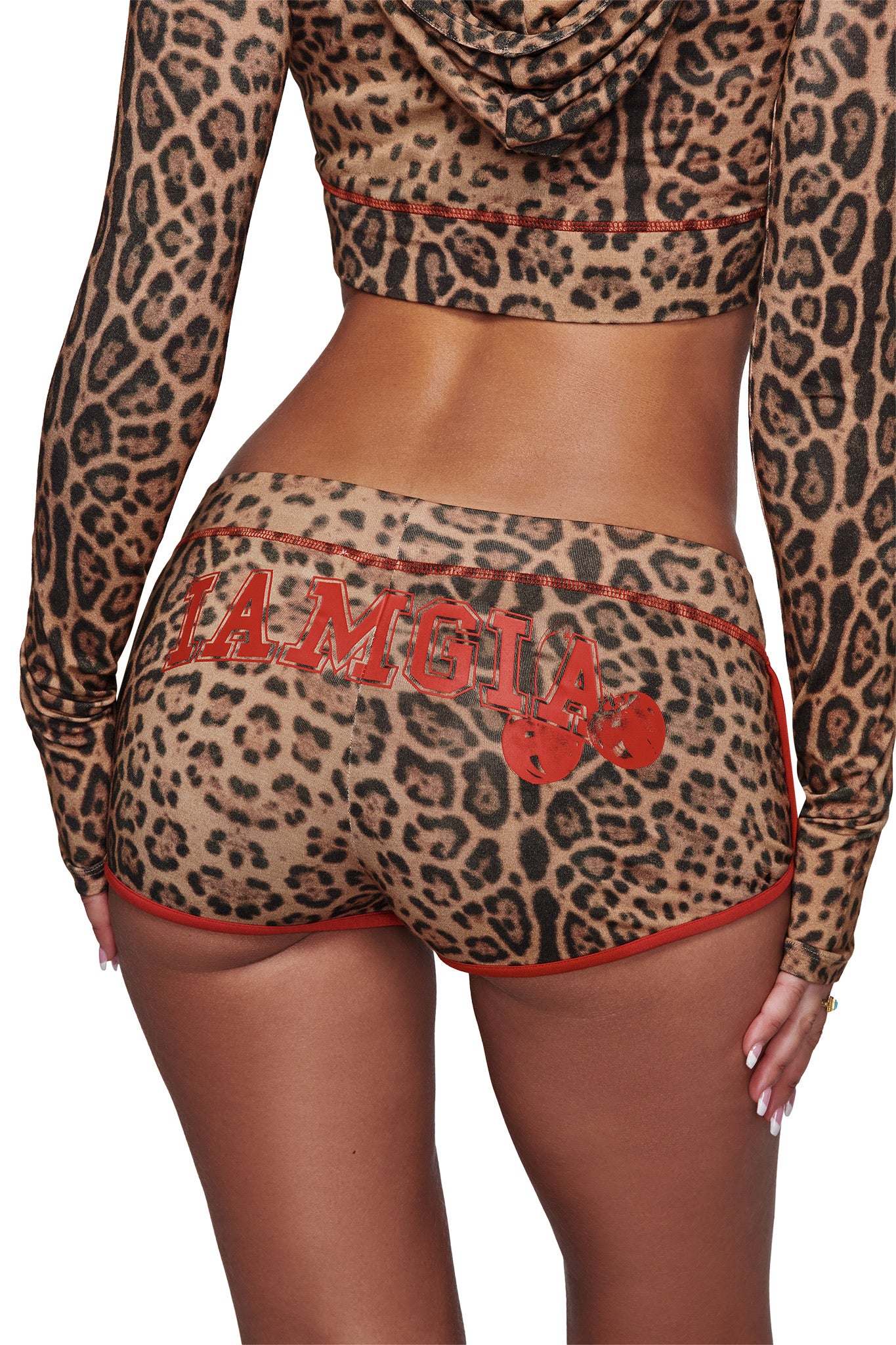 A person is seen from behind wearing a leopard-print outfit featuring the I.AM.GIA BLARE DOLPHIN SHORT - PANTHERA with “I.AM.GIA” and two red boxing gloves printed on the shorts; the top includes long sleeves and a hood.