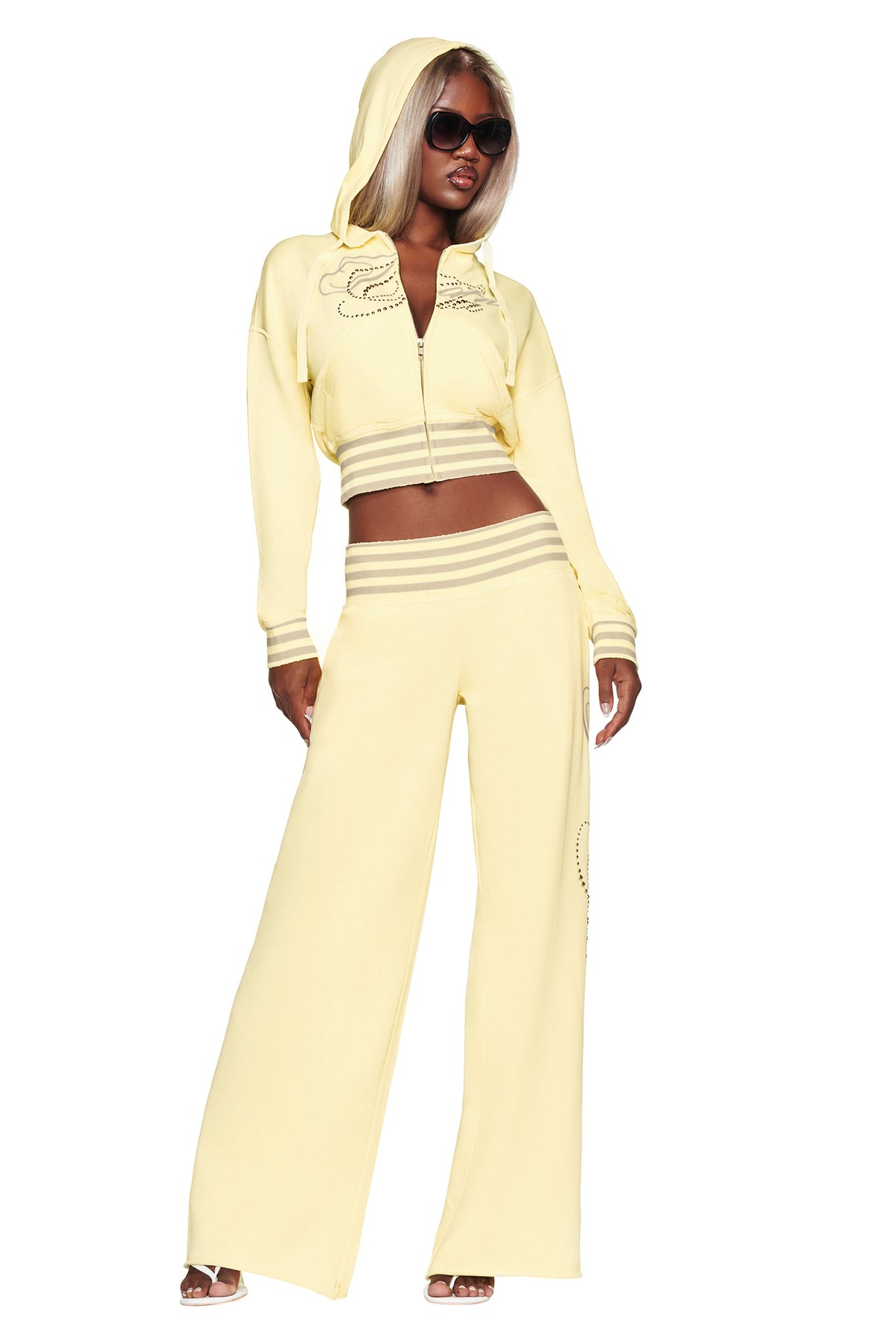A woman wearing sunglasses and the I.AM.GIA VEDA JACKET in yellow, with the hood up, paired with matching yellow wide-leg pants, posing confidently.
